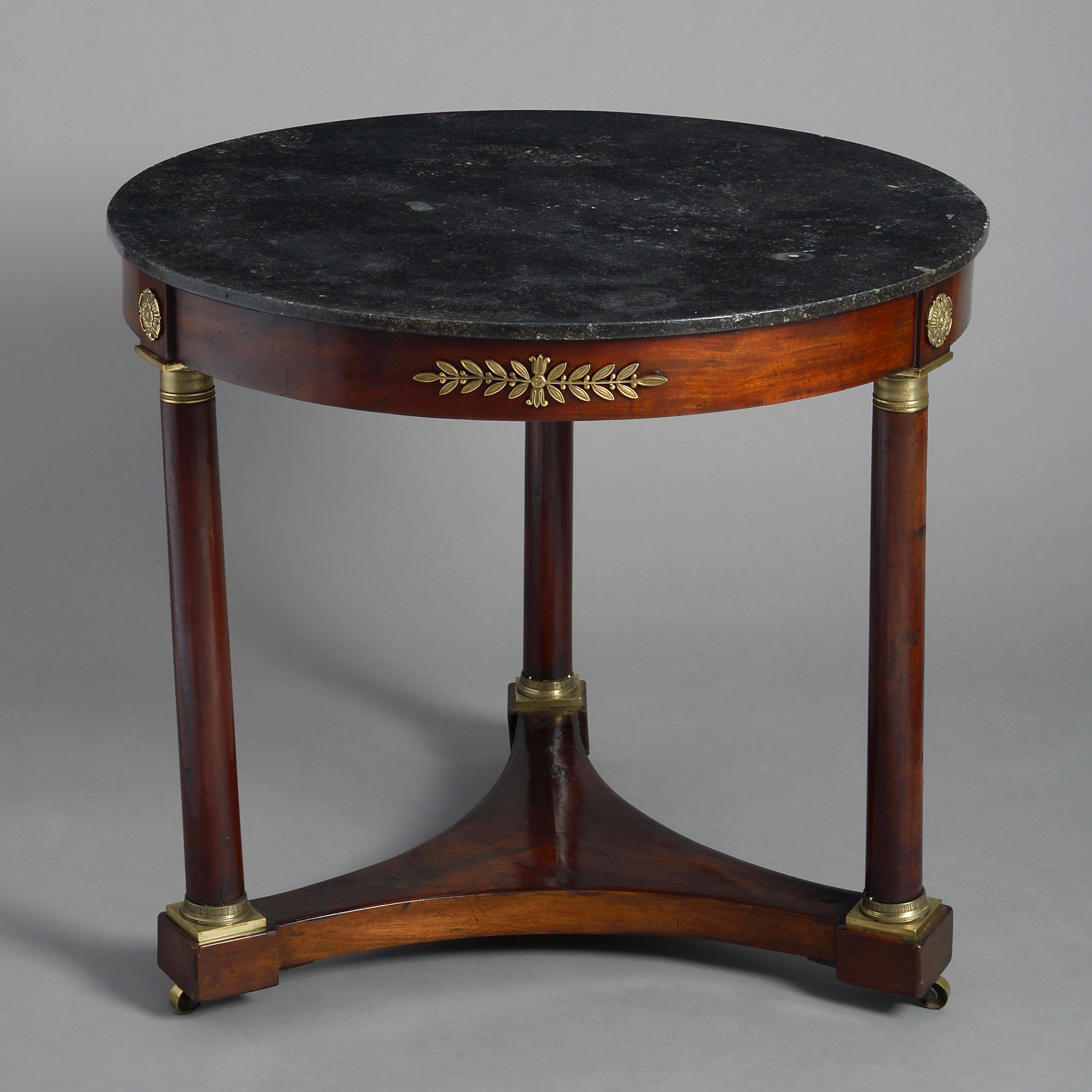 An early 19th century Empire period mahogany centre table, the grey marble fossil top set upon a frieze with brass mounts in the classical taste and supported by three columns with fine engine turned capitals and socles, all set upon a concave base