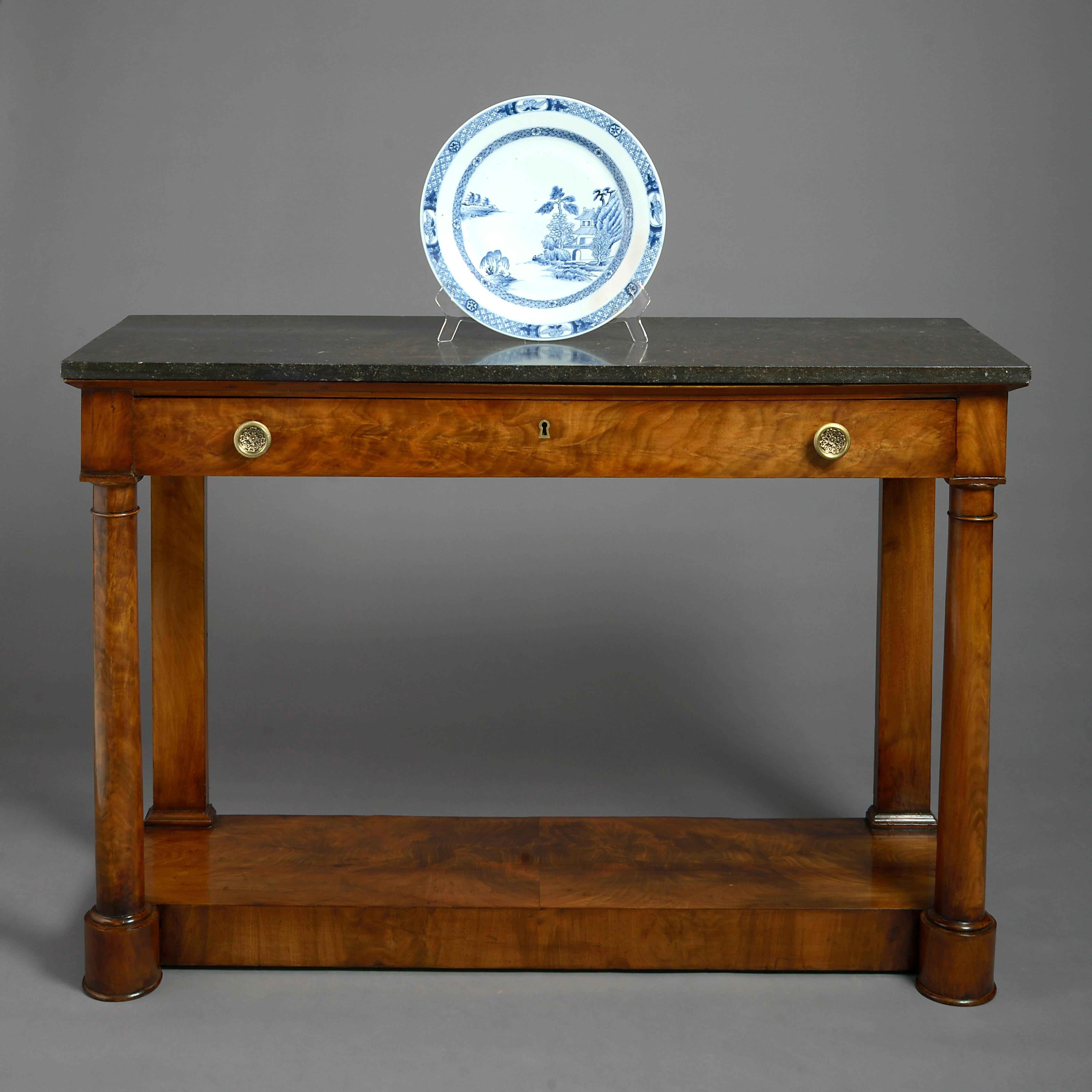 A fine early 19th century Empire period figured mahogany console table, the rectangular black fossil marble top above a single drawer with finely cast and chased circular brass handles, all set upon two turned columns and rear pilaster supports,