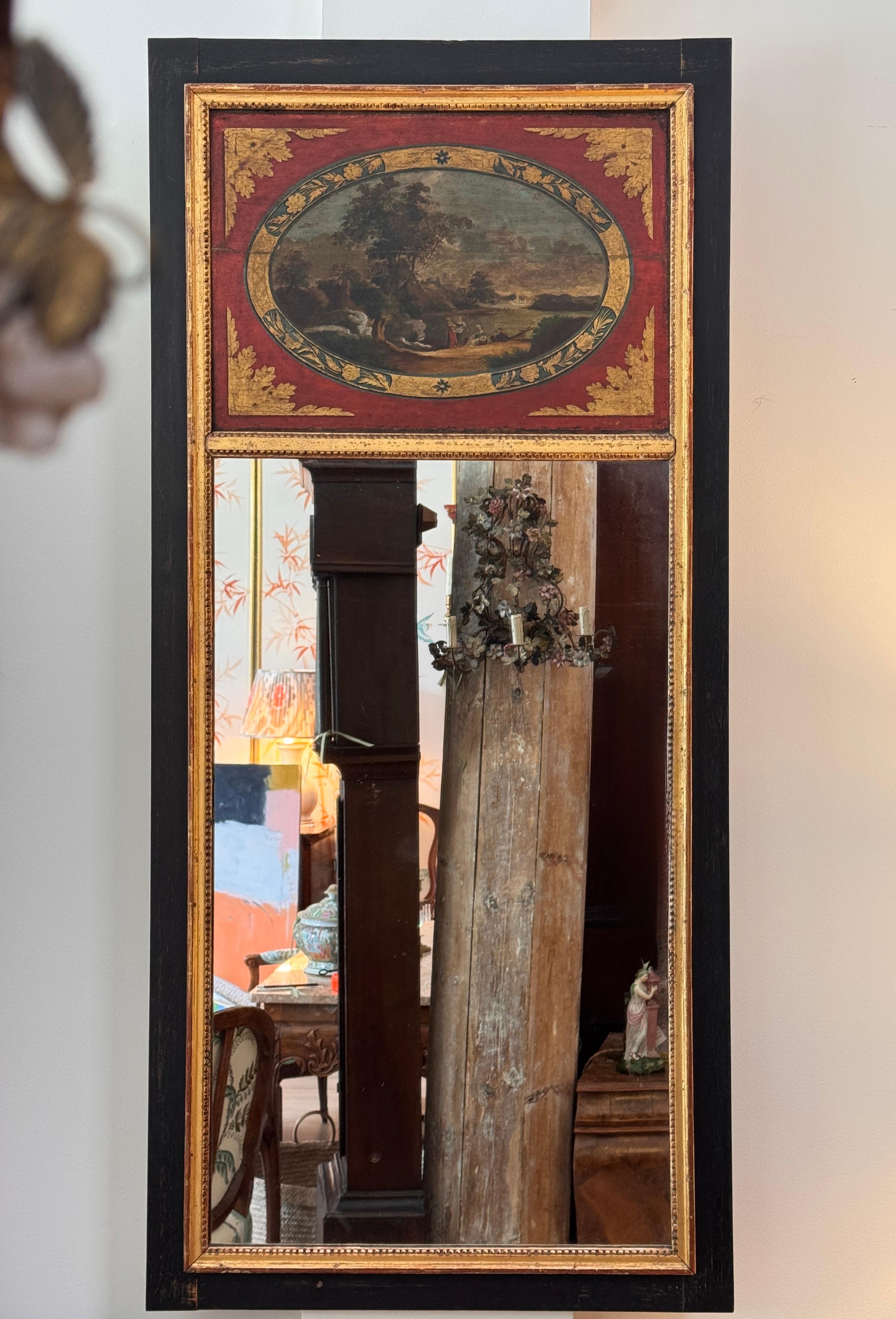 Miroir anglais du début du 19e siècle avec cadre laqué noir et panneau richement peint au-dessus de la vitre. La partie supérieure présente un paysage pastoral classique entouré d'une réserve ovale avec une bordure feuillagée dorée, le tout sur un