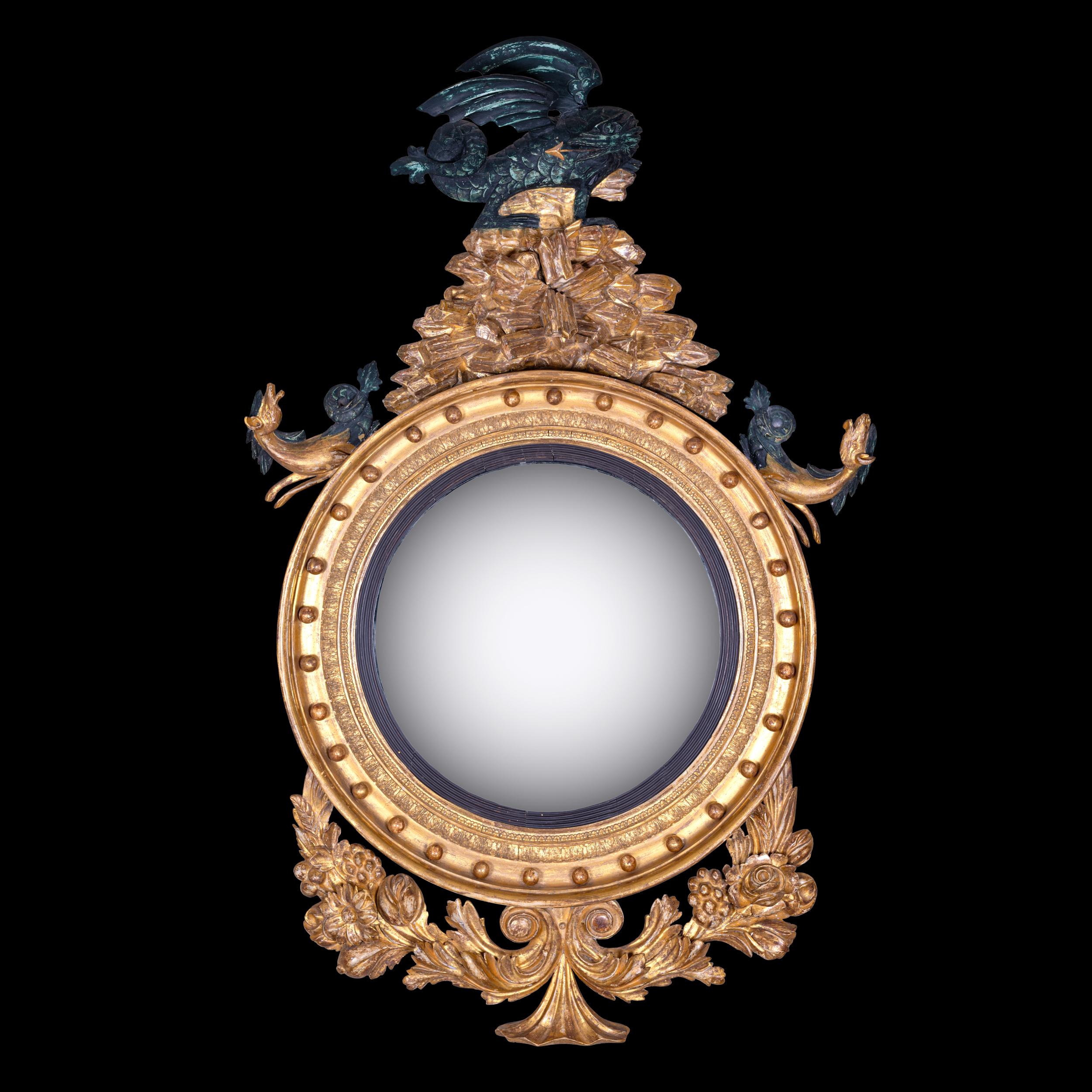 Espejo convexo muy llamativo e imponente. La placa circular del espejo está dentro de un marco ebonizado, con decoración foliada y esférulas aplicadas, coronado por un dragón que escupe fuego encaramado a un lecho de rocas, flanqueado por