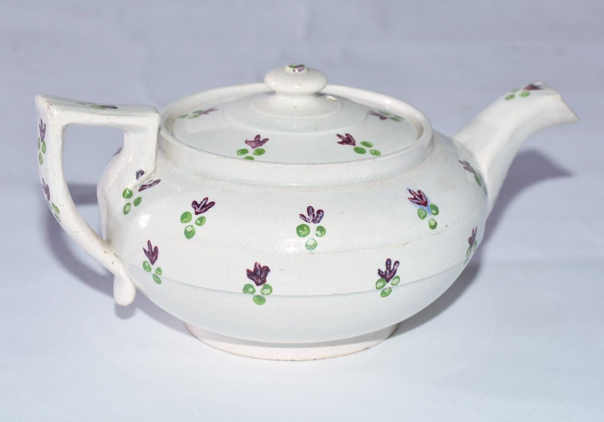 The early 19th century English creamware child-size teapot is handcrafted and hand-painted with tiny stylized purple leaves and green berries. The teapot is made of soft-paste pottery. There are holes inside the teapot to restrain tea leaves when