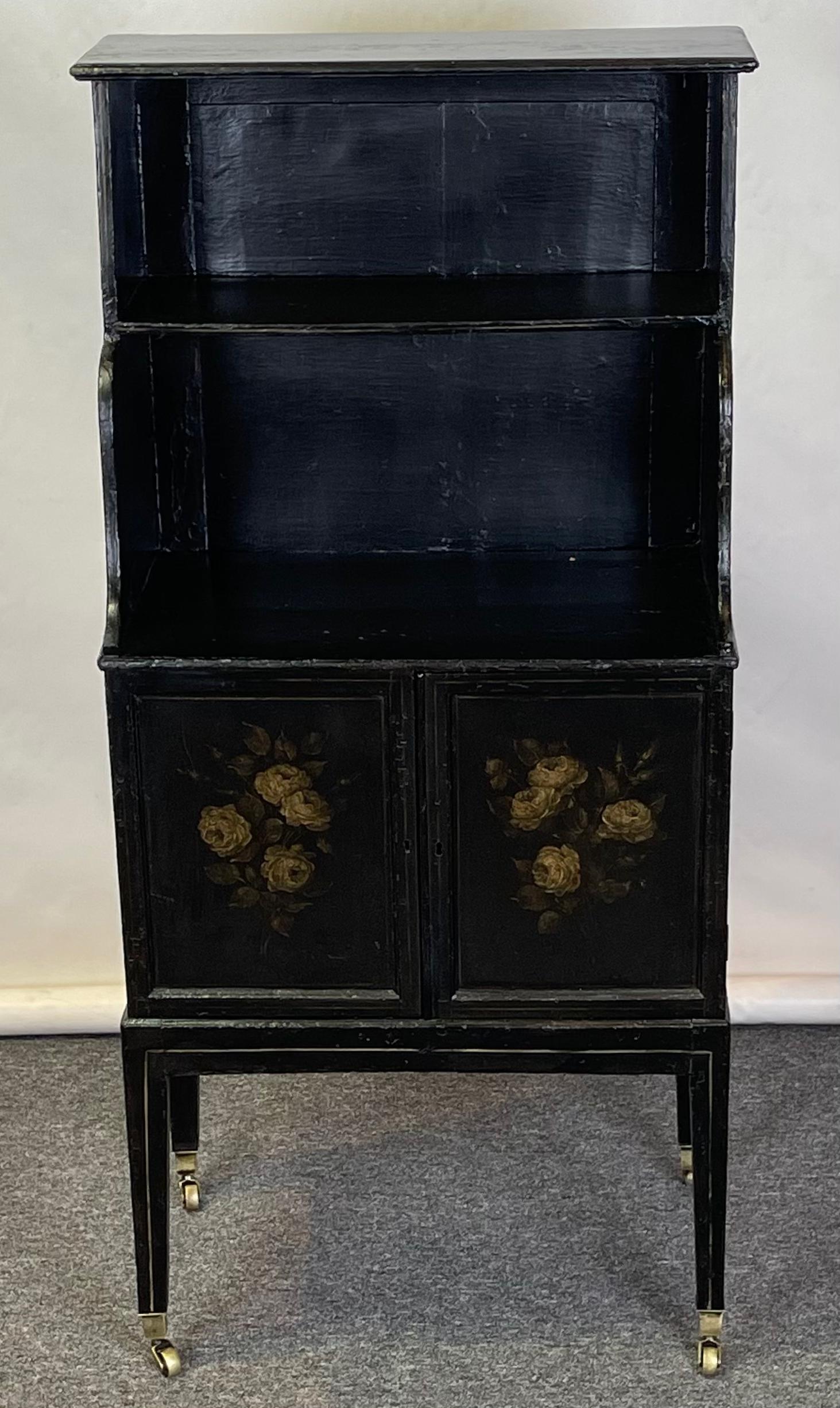 An small and charming early 19th C. English ebonized and paint decorated two-shelf bookcase cabinet on square tapering legs terminating in brass casters.
