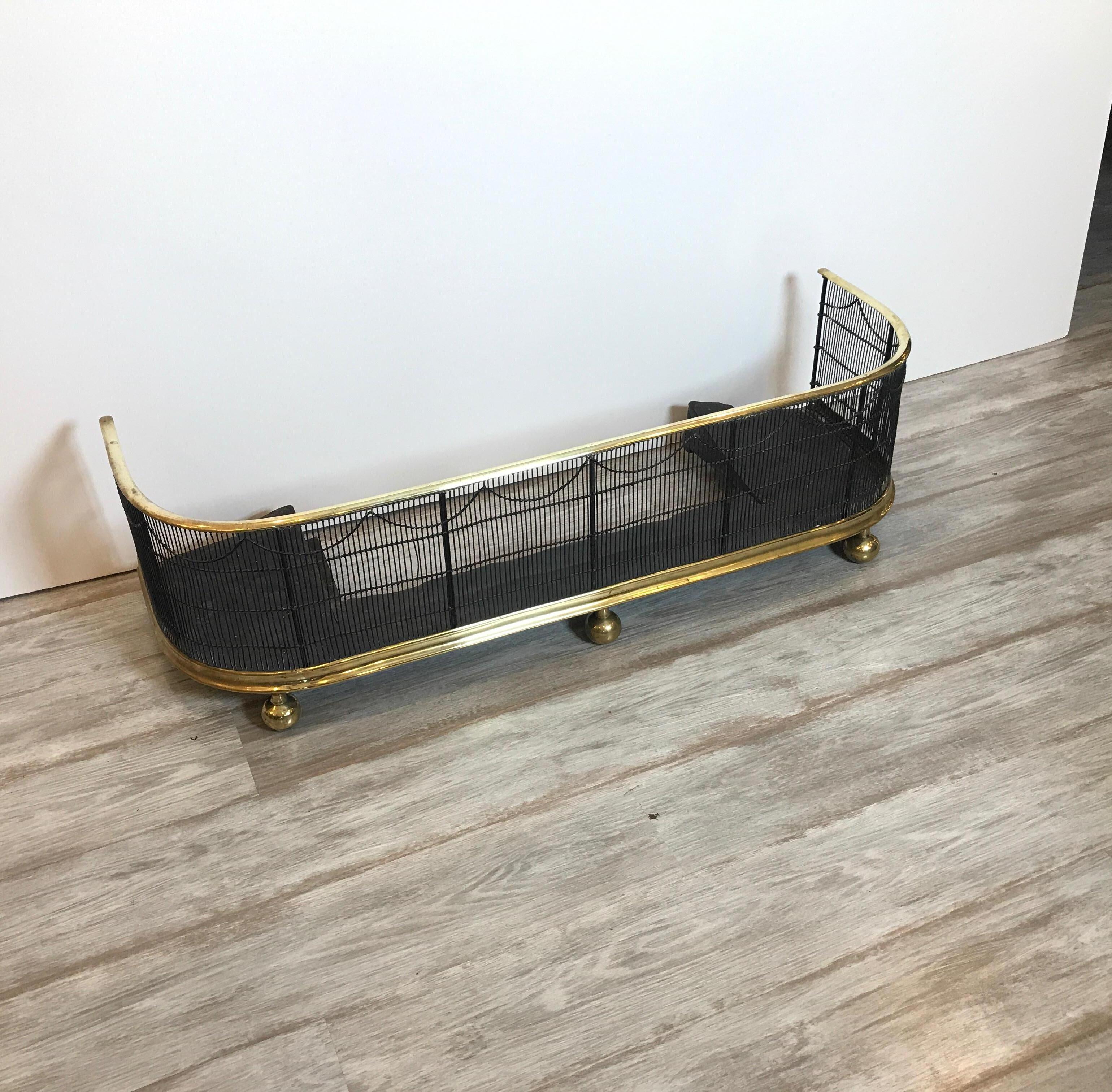 An early English Regency brass and wire fireplace fender. The fender with polished brass top rail and bottom rail with brass bun feet. The wife fender in its natural dark aged finish.