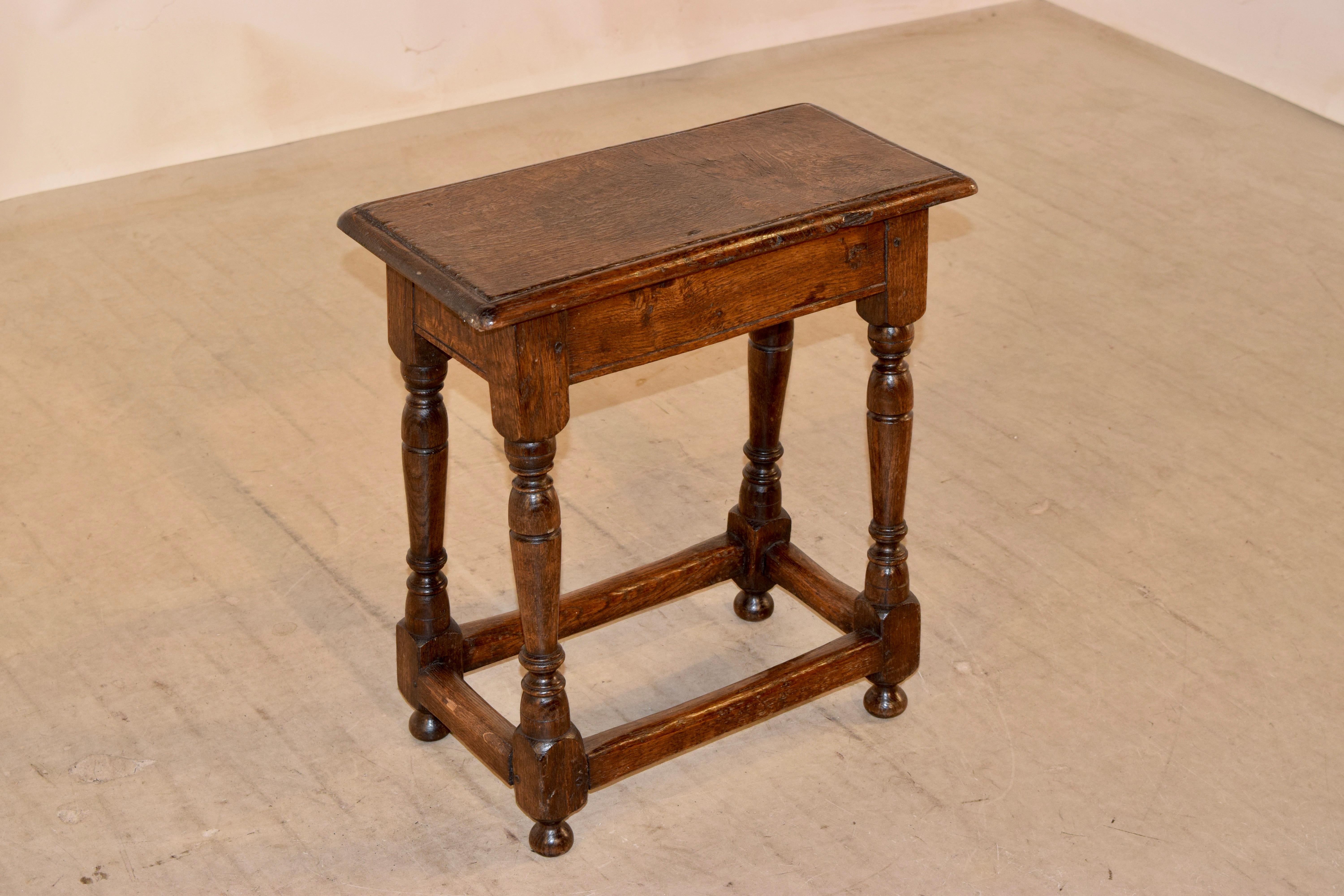 Early 19th century oak joint stool from England. The top has a beveled edge, following down to a simple apron and supported on hand turned splayed legs, joined by simple stretchers and raised on hand turned feet.