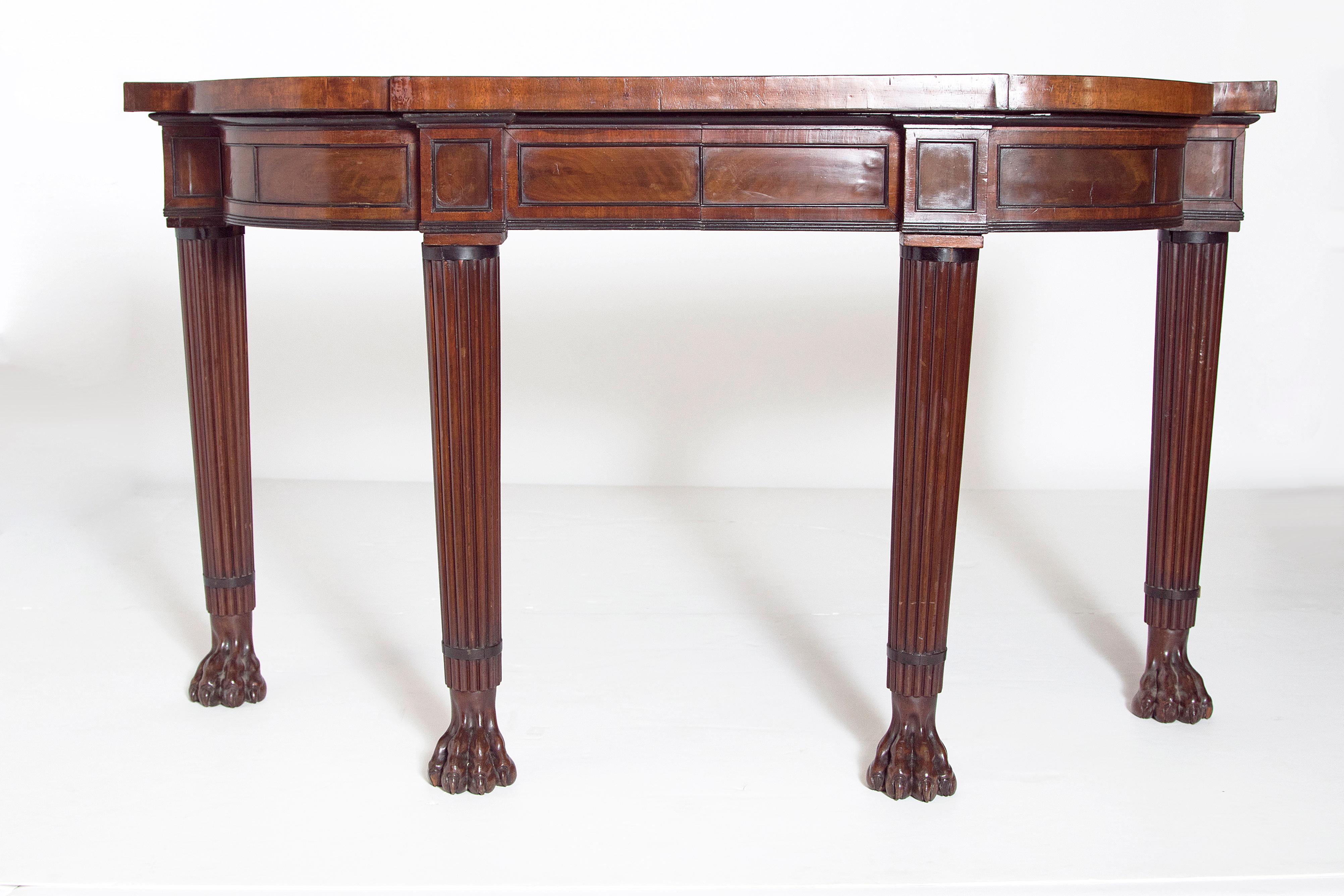 English Regency console table of mahogany with a shaped top and apron. Supported on four round reeded legs terminating in large paw feet.