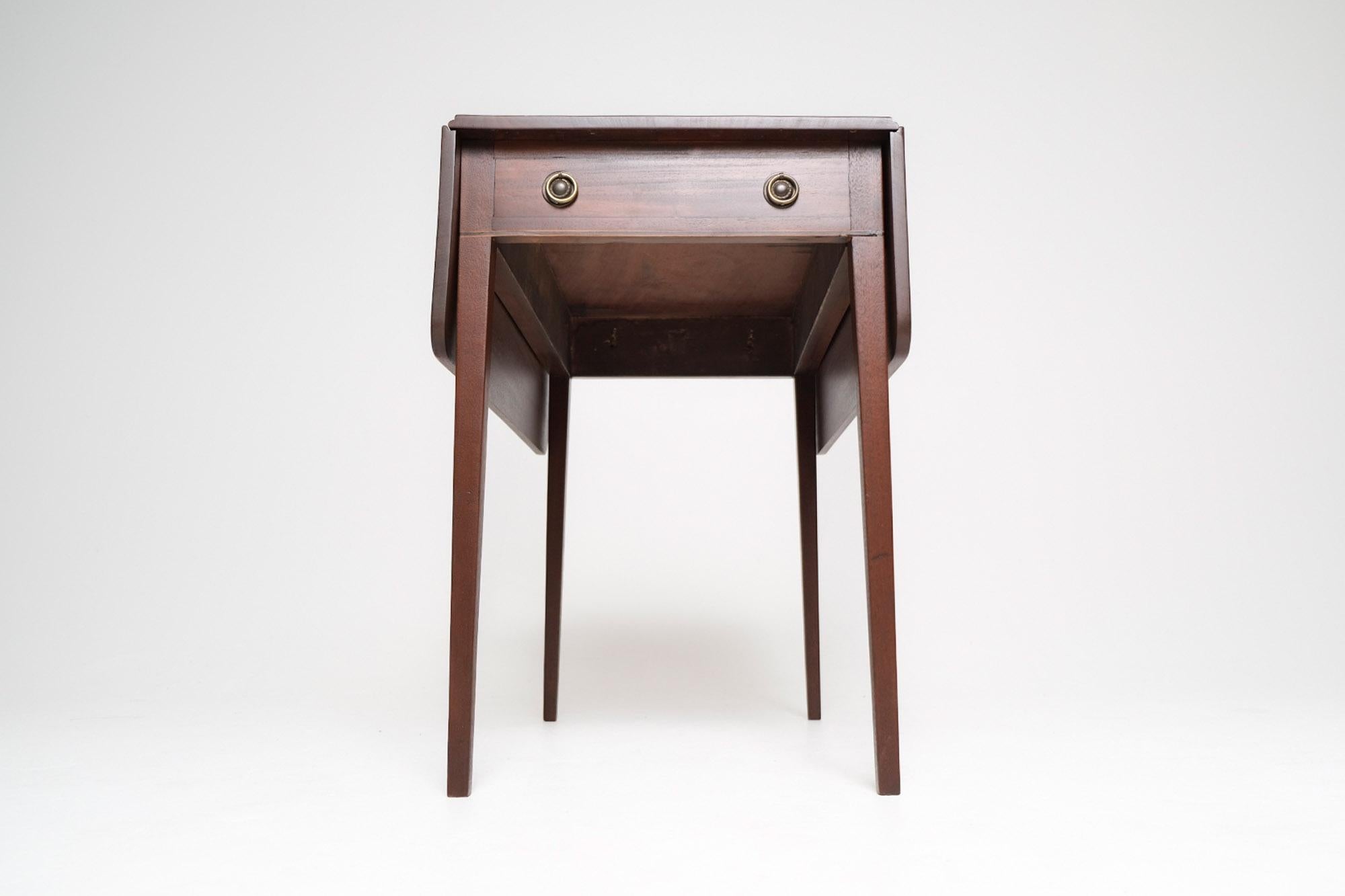 A refined early 19th century English Pembroke table in solid mahogany, notable for its restrained Regency-era design and clean proportions. The rectangular top features two drop leaves supported by swing-out wooden brackets, offering flexible use as