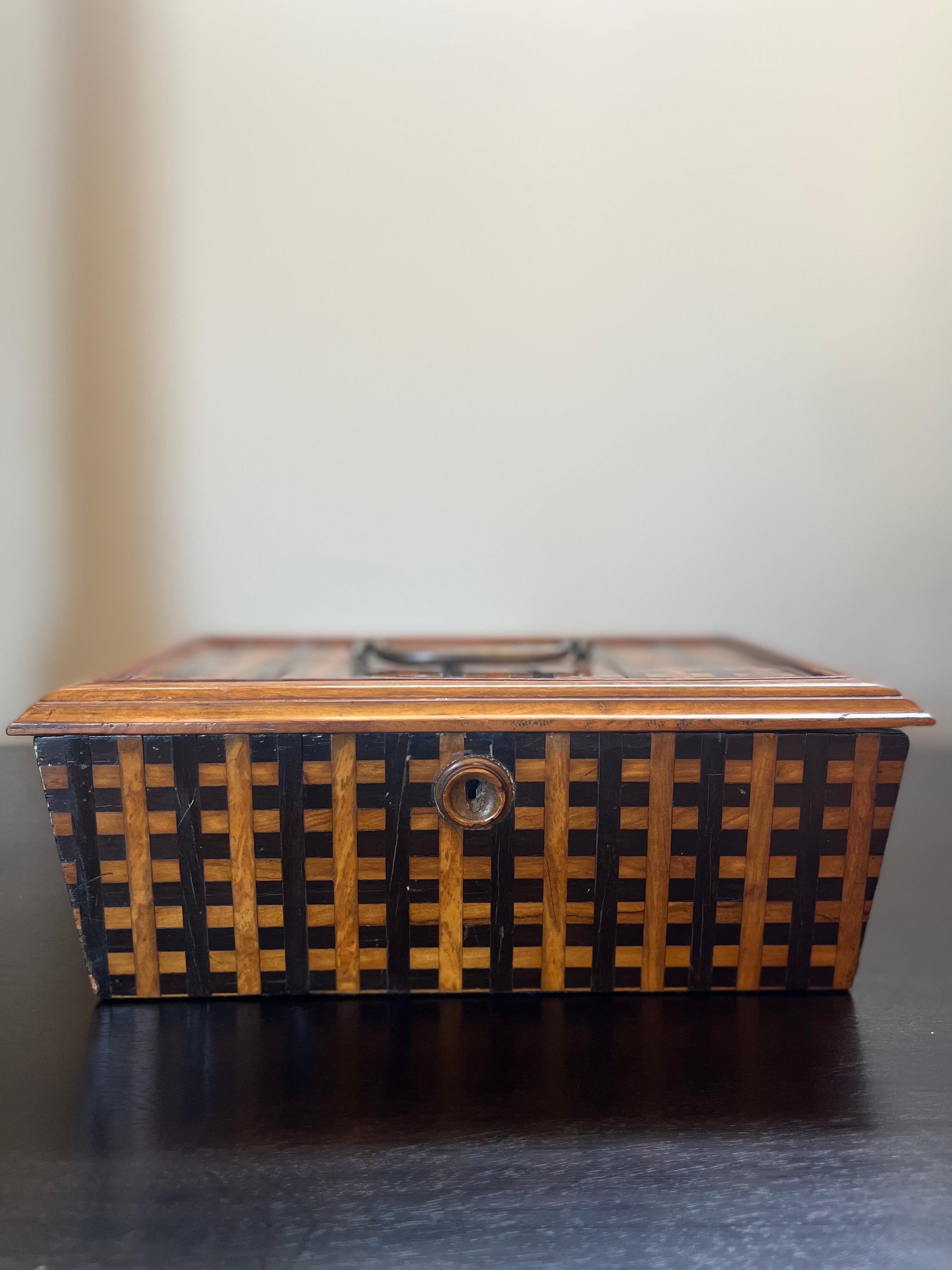 Georgian parquetry box featuring two-toned woven lattice pattern, metal carrying handle, hinged lid and wooden keyhole. Lined with red velvet, this piece of early 19th century English woodwork makes a discreet yet elegant storage unit, as well as