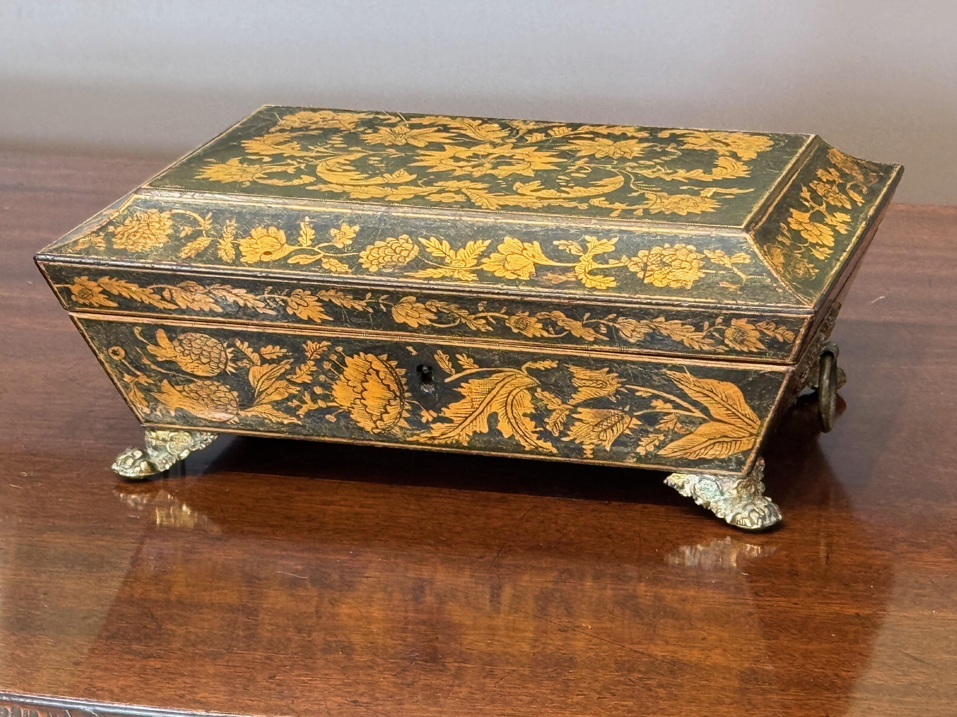 A finely decorated early 19th century English penwork box featuring delicate floral and foliate motifs throughout. The rectangular case rests on four cast metal paw feet and is fitted with ring handles at either end. Interior lined in vibrant red