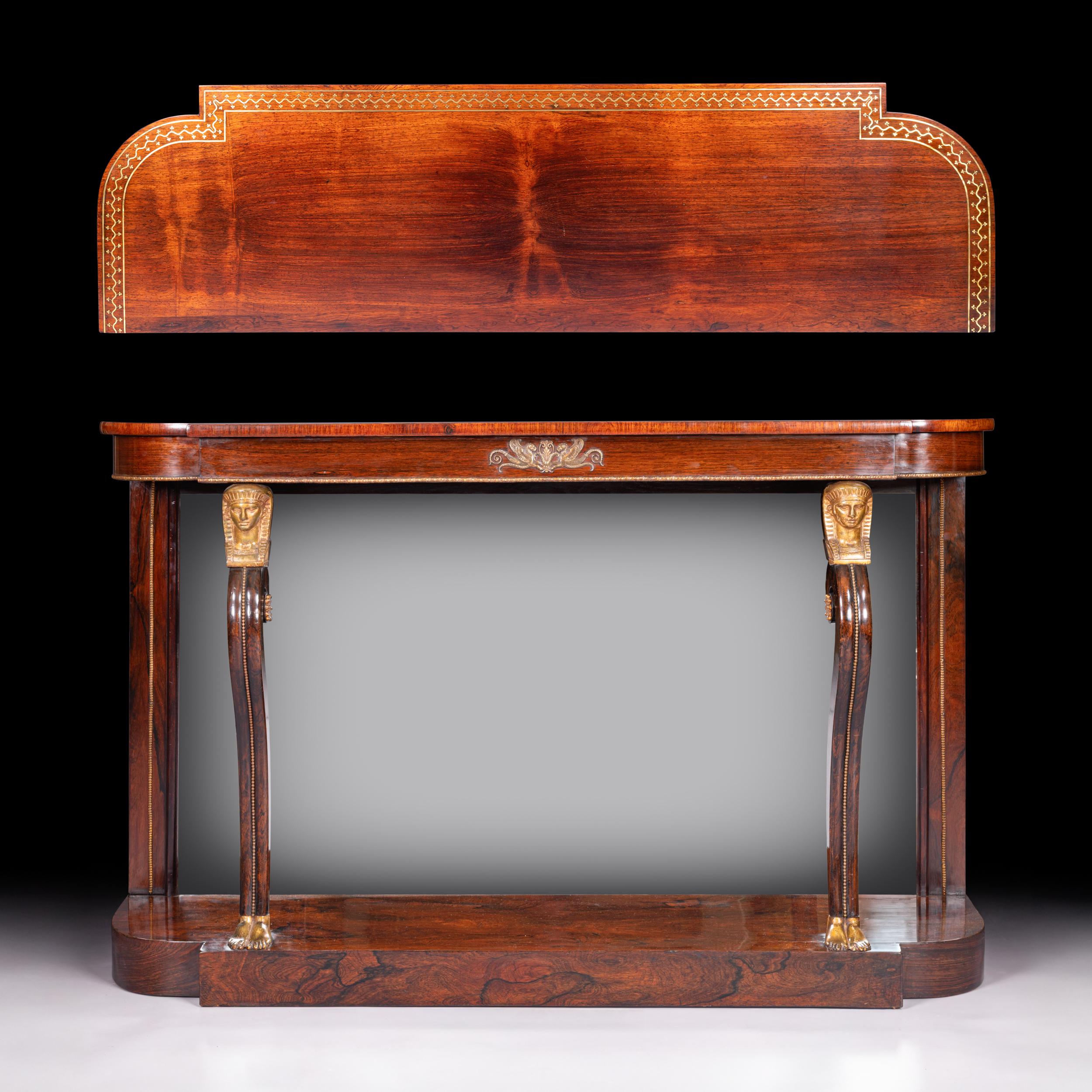An outstanding Regency period console table in beautifully figured rosewood, enriched with finely cast and gilded bronze mounts in the Egyptian Revival taste. The rectangular top with rounded front corners is banded in rosewood and bordered with