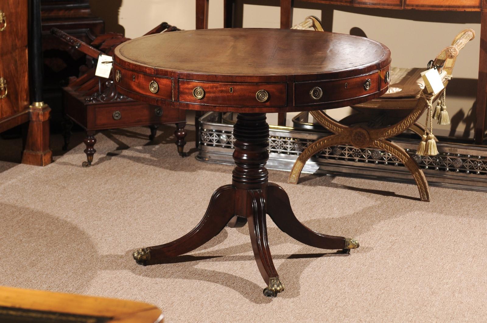 The Regency drum table with brown leather top, 4 sliding drawers and 4 false drawers, turned pedestal below terminating in 4 splayed legs with brass paw castors. 

 