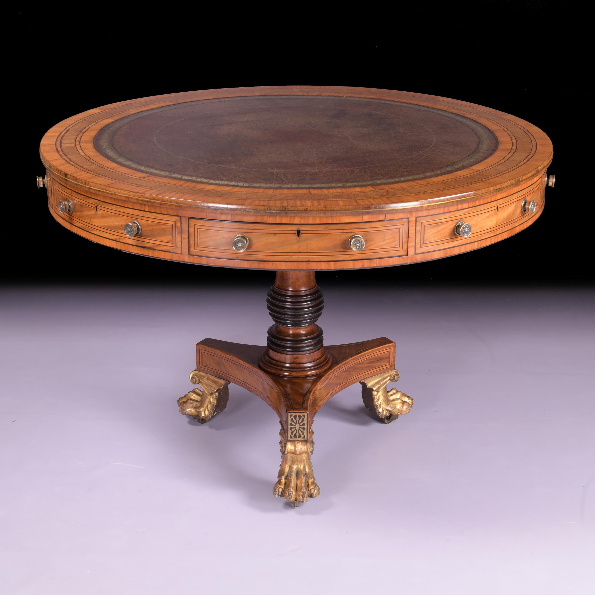 An exceptional early Regency Satinwood and line inlaid revolving drum/centre table, with a gilt-decorated brown leather-lined top above four frieze drawers and four dummy drawers, on a column support, on a concave-sided triform platform, with gilt