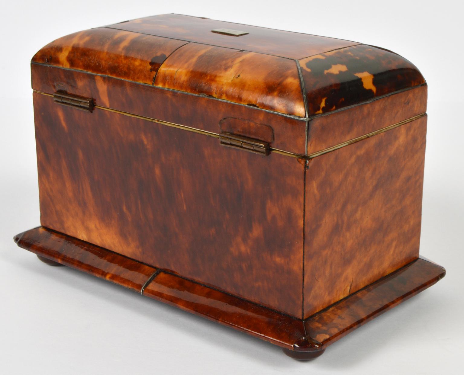 A fine English regency silver stringed tortoise shell tea caddy with architecturally shaped front, matching domed top and skirted body resting on mahogany bun feet. The top opens up to an interior fitted with two foil lined compartments, tortoise