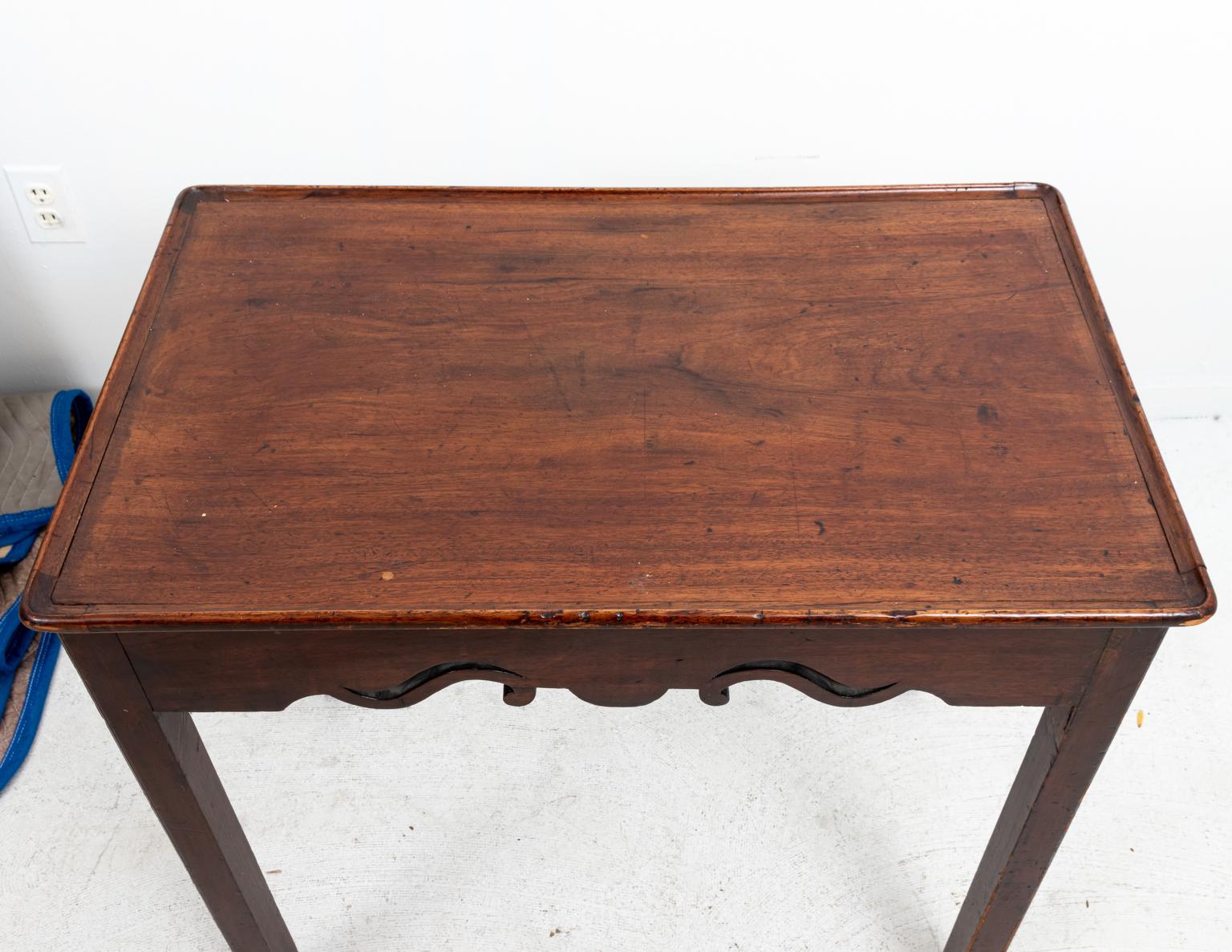English tea table in Mahogany, circa 1810s. The piece is in the Chippendale style with pierced, carved apon and tray top resting on four straight square turned legs. Made in England. Please note of wear consistent with age including slight