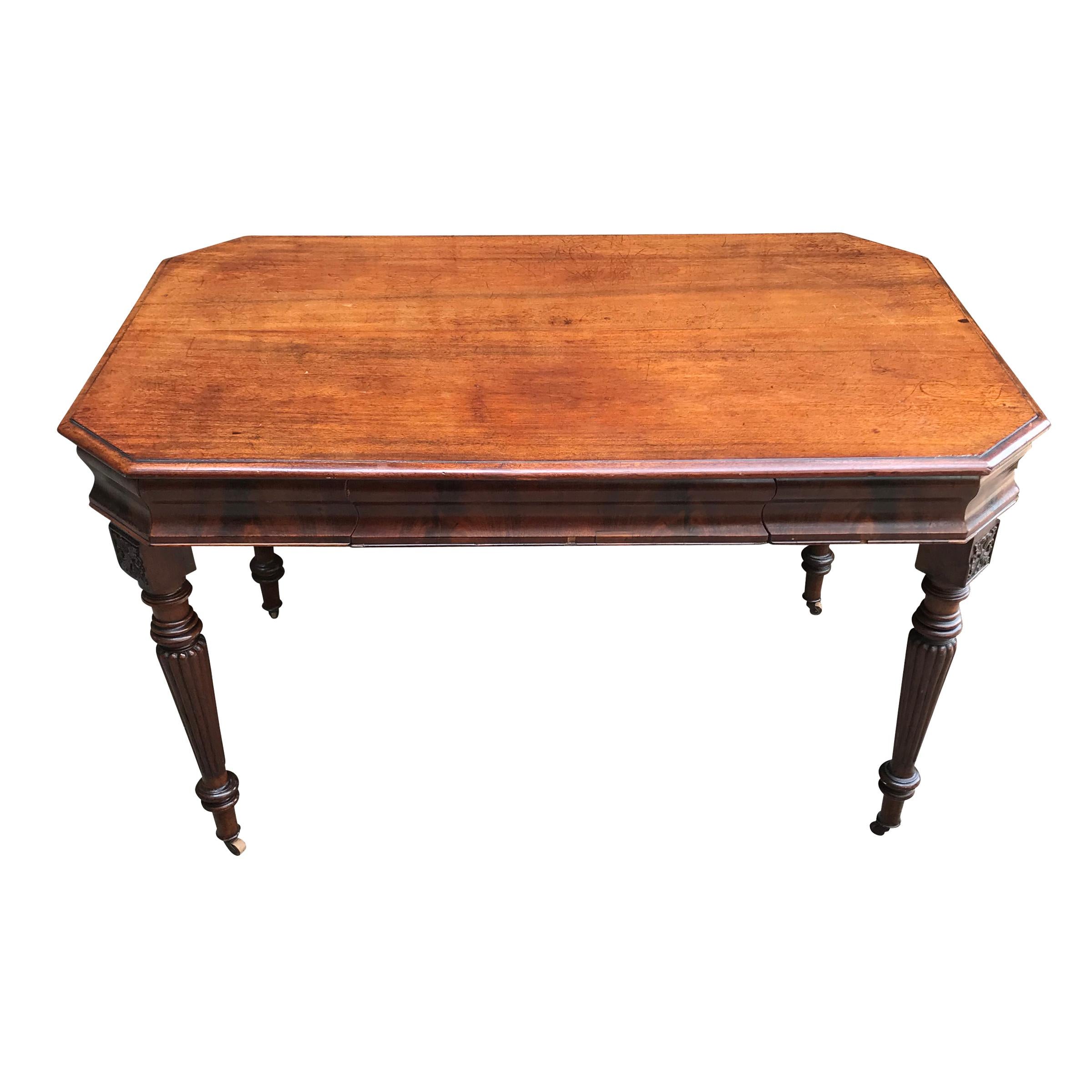 A 19th century English early Victorian period mahogany writing table or desk with a hexagonal top composed of two wide mahogany planks with a simple rounded edge detail. The apron is flame mahogany veneer, with one large drawer in the center. The