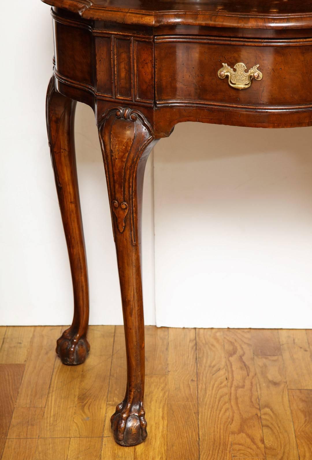 A pair of early 19th century walnut demilune console tables, the top with molded edge resting on a waved apron with foliate escutcheons, the slight cabriole legs terminating in claw and ball feet, French polish finish.