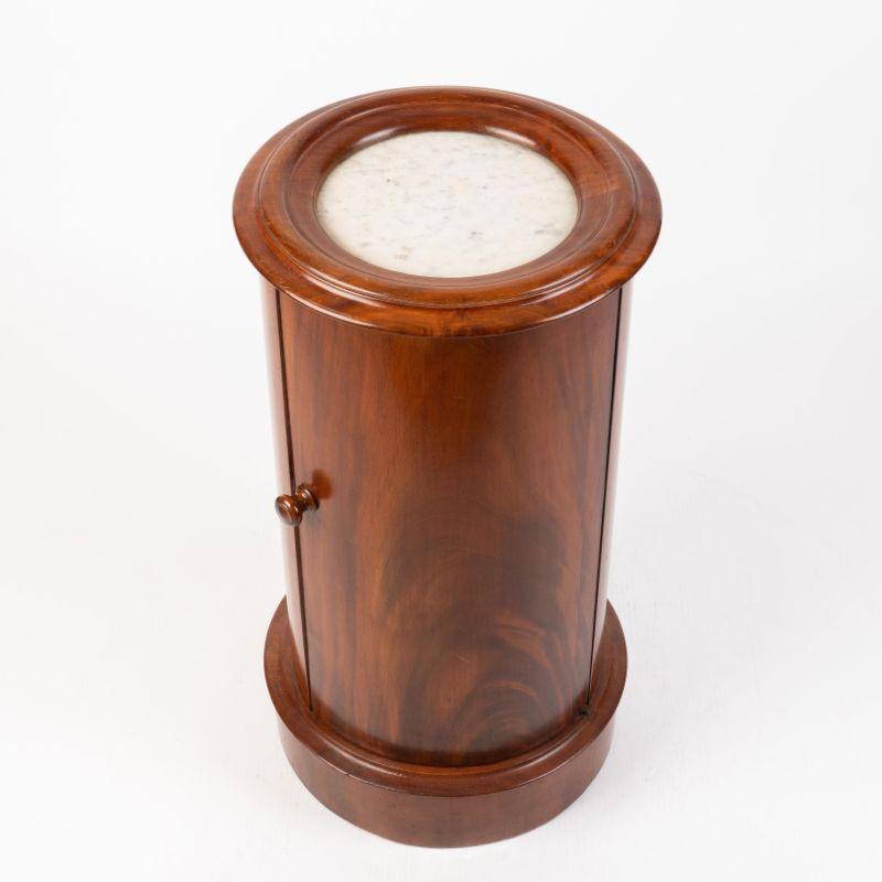 William IV mahogany pillar commode with white marble top framed by a bolection molding. The column rests on a base board molding with castors and is fitted with a blind door and turned mahogany knob. The interior is fitted with a single