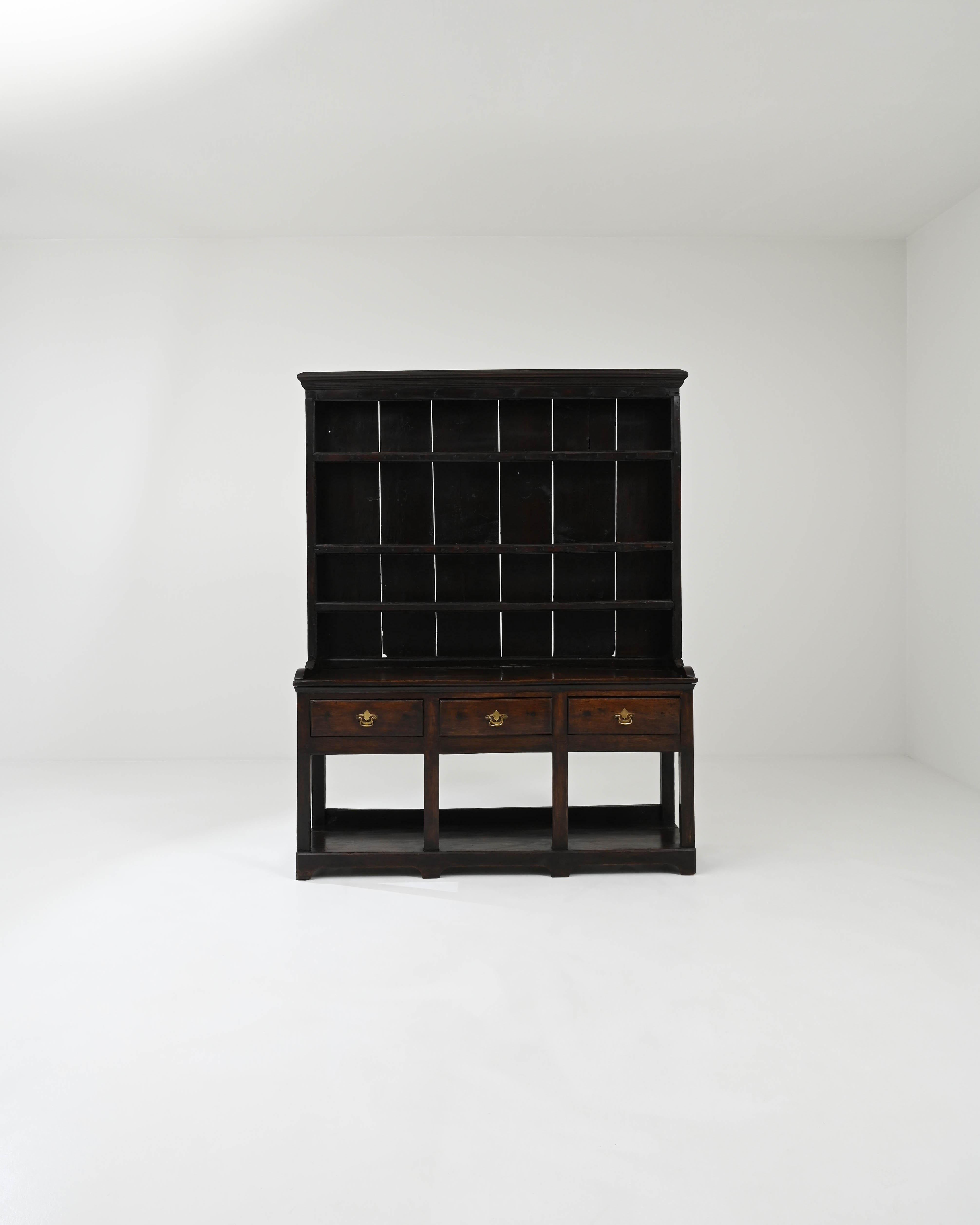 A wooden cupboard created in early 19th century England. Dark and dramatic, this country cupboard exudes a sense of history and traditional beauty and eloquence. The dark glowing, moody hardwood emits a curious luster, which bonds in tasteful