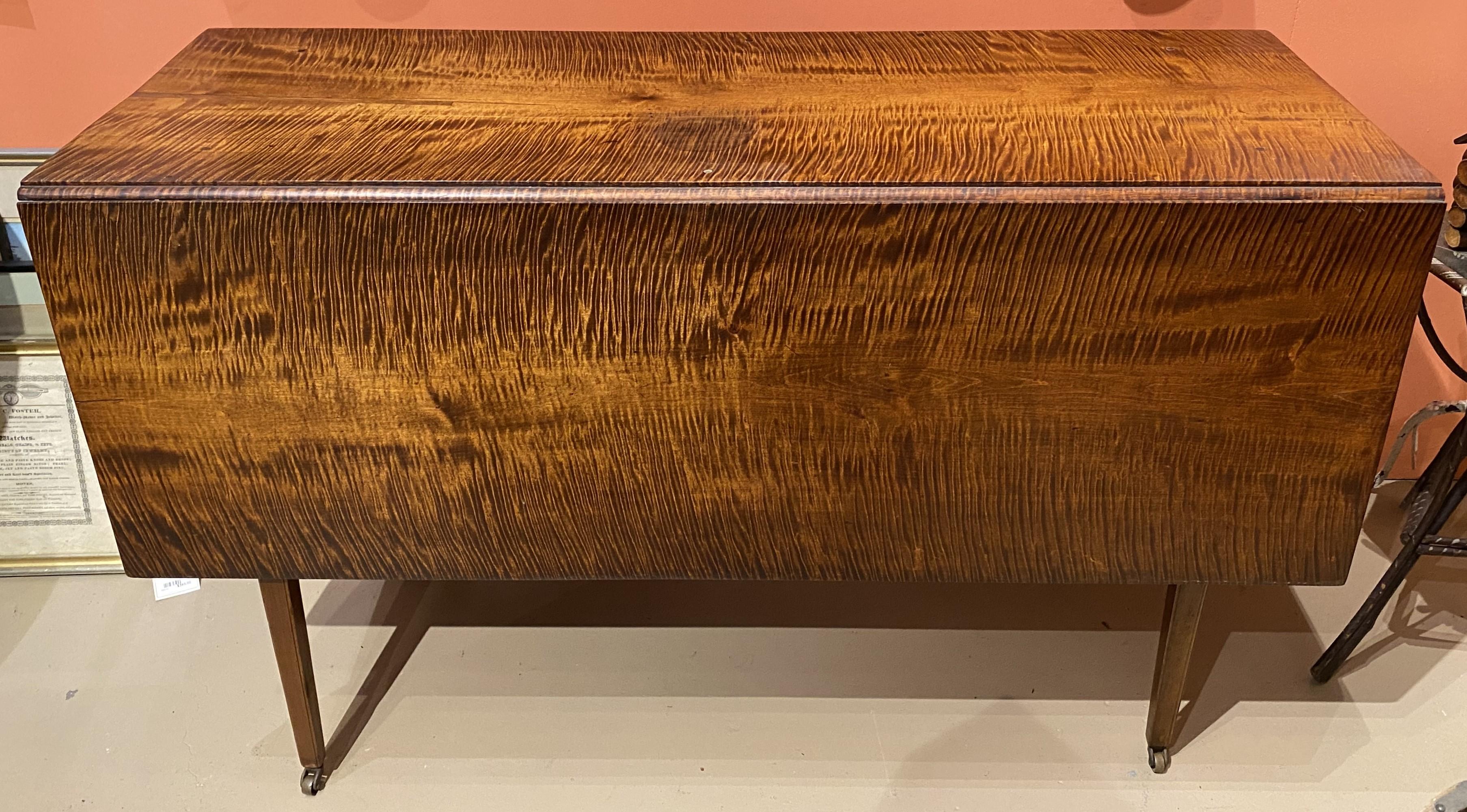 A Federal tiger maple drop leaf dining table with bold wood grain, tapered square legs terminating with brass casters,  and dovetailed construction. Very good overall condition, with  great overall patina, minor top ring stain and shrinkage repairs.