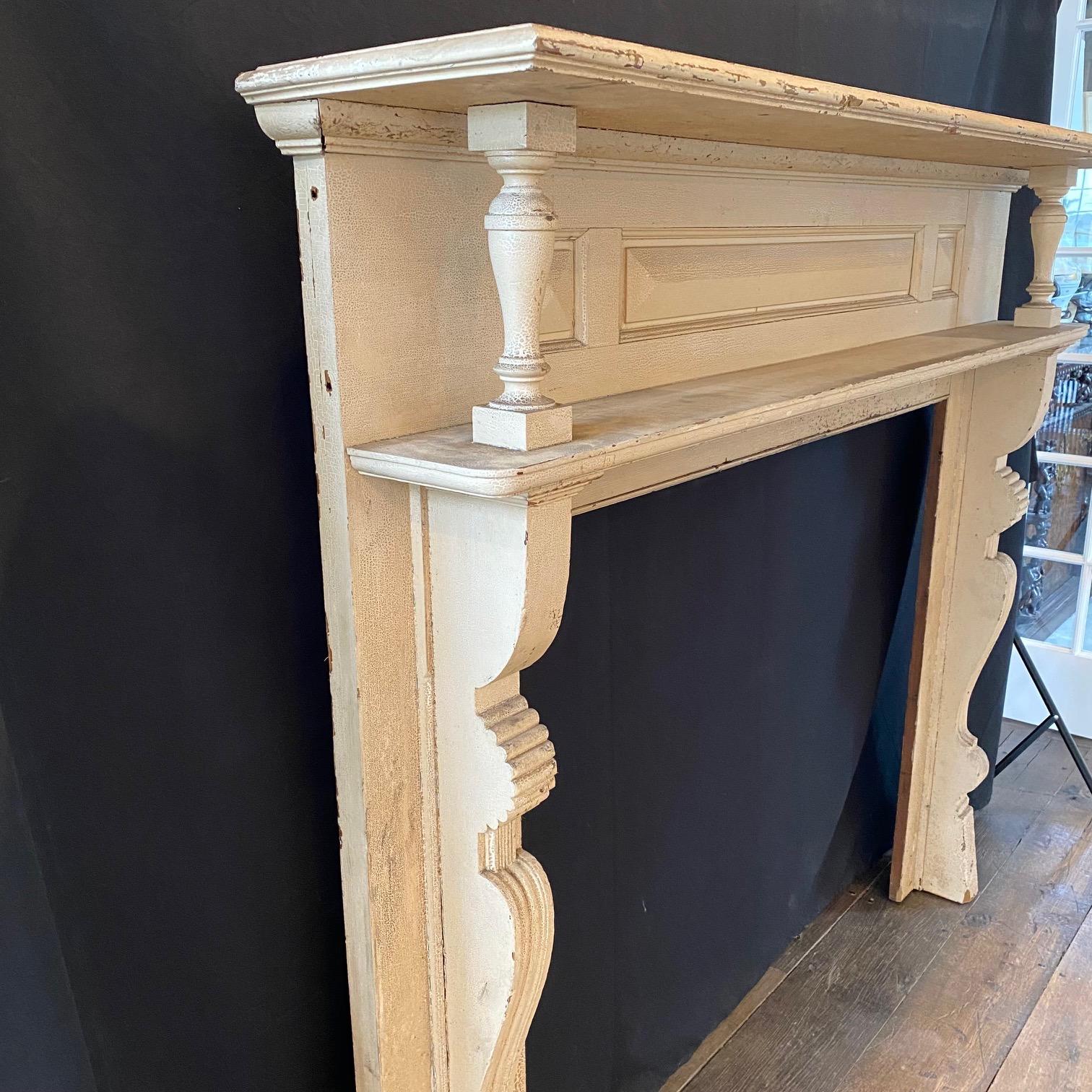 Crafted in the Federal style with a striking paneled frieze and light cream paint finish, this antique fireplace mantel brings elegance, and also adds some Arts and Crafts era touches in its carved details. The simple and unassuming design is truly