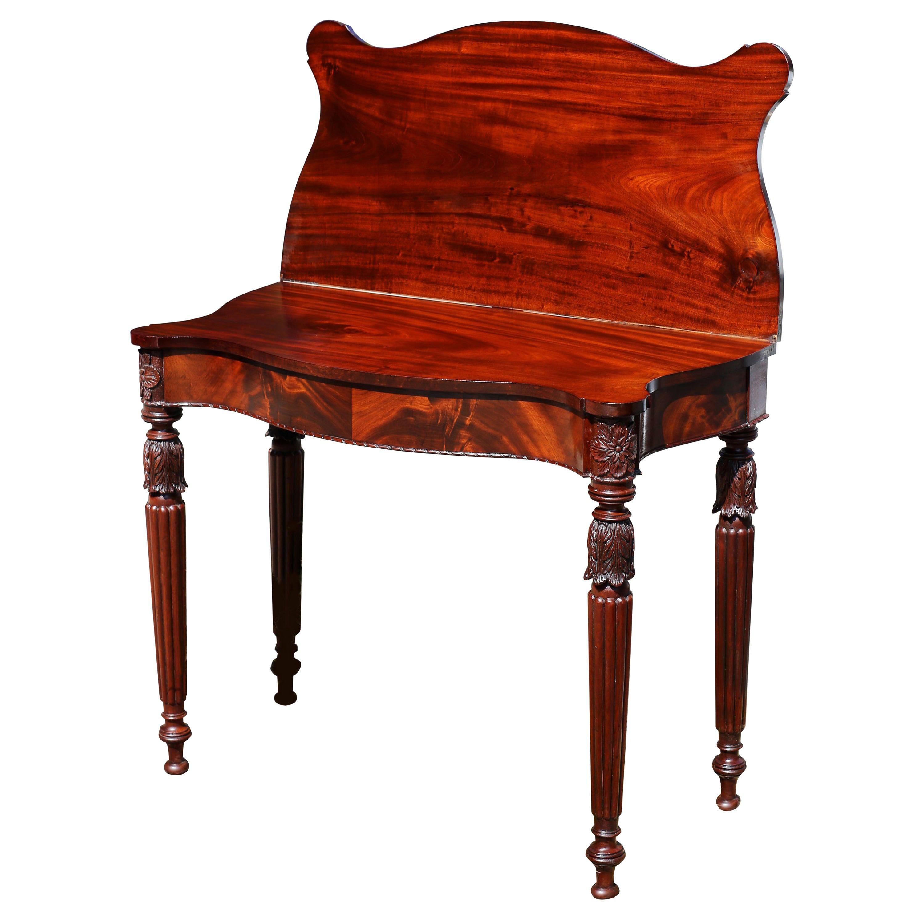 A stunning Sheraton card table of magnificent figured Cuban mahogany, this piece exhibits the finest qualities of Salem, Massachusetts shop of cabinetmaker or architect Samuel McIntire. A flip-top bow front slab table with scalloped corners is