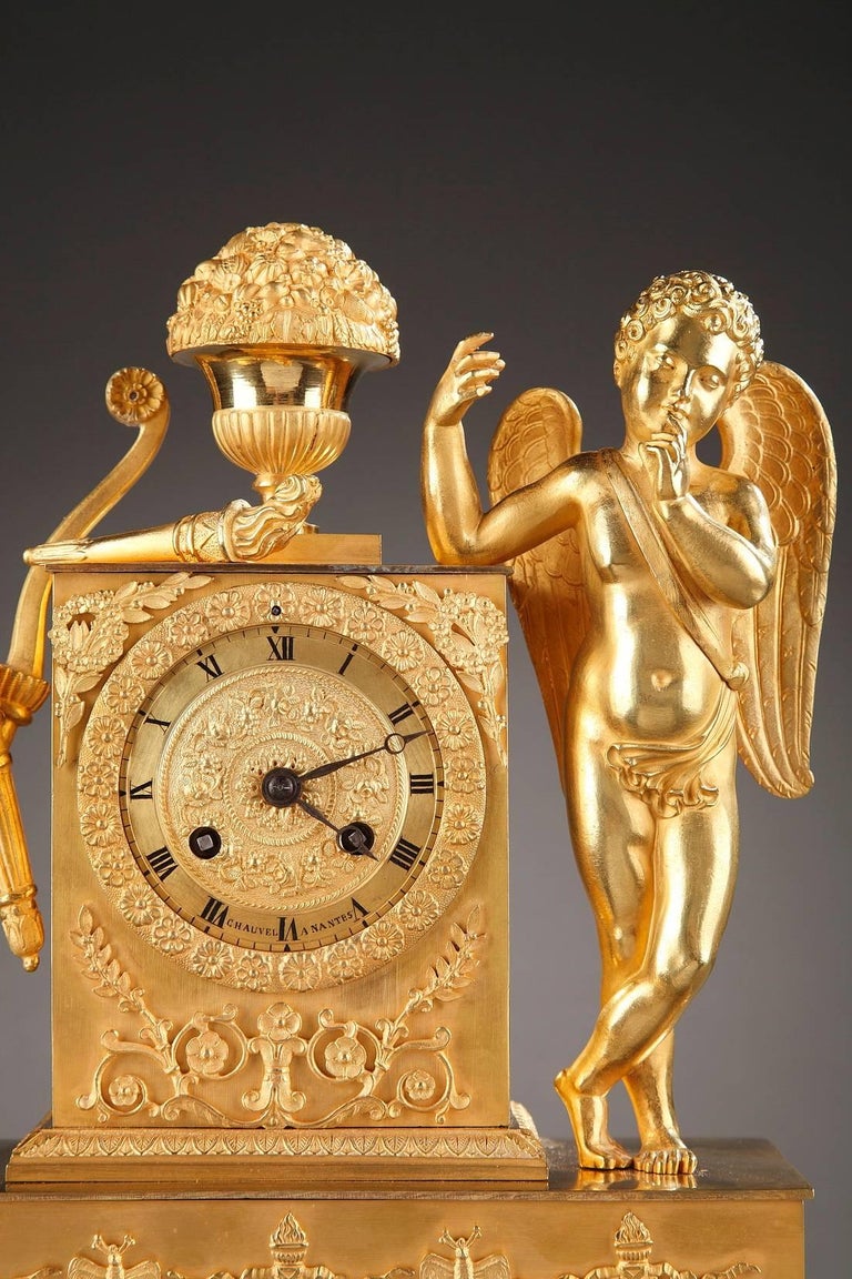 Exquisite sculpted and gilded mantel clock with a young cupid. He is leaning against a column that is intricately sculpted with crowns, laurel branches, and winding foliage. The ormolu dial is decorated with friezes of flowers on a matte background.