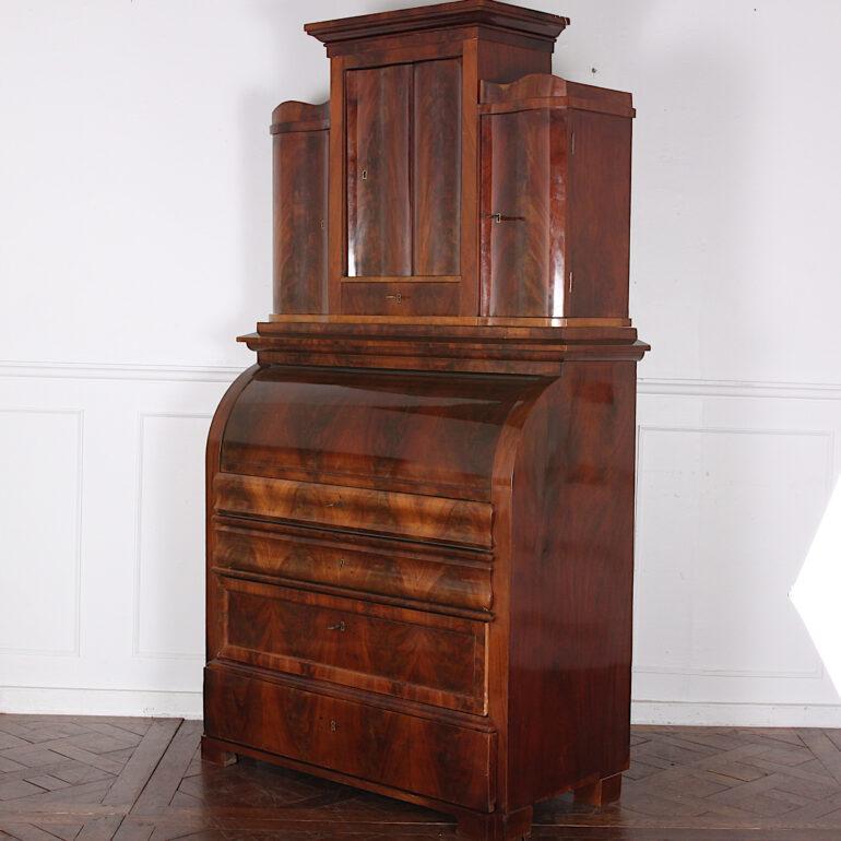 A German ‘Biedermeier’ secretary in flame mahogany, the cylinder roll opening to an interior with drawers and inlaid cabinet above a pull-out writing surface with further compartments. Upper cabinet with three cupboards behind shaped flame