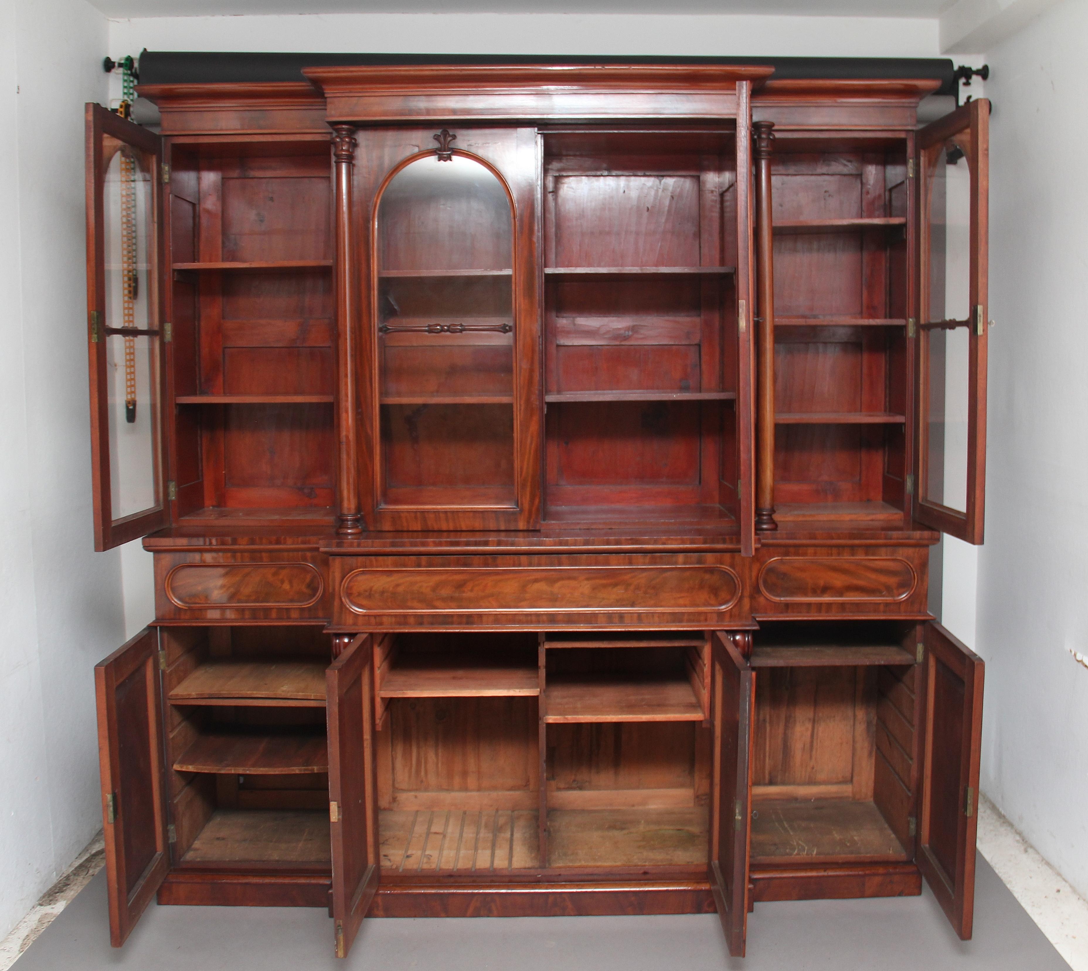 Early 19th century flame mahogany breakfront bookcase, the molded cornice above four arched glazed doors, with carved decoration at the top of each door and a turned and carved spindle at the centre, the middle doors flanked either side by