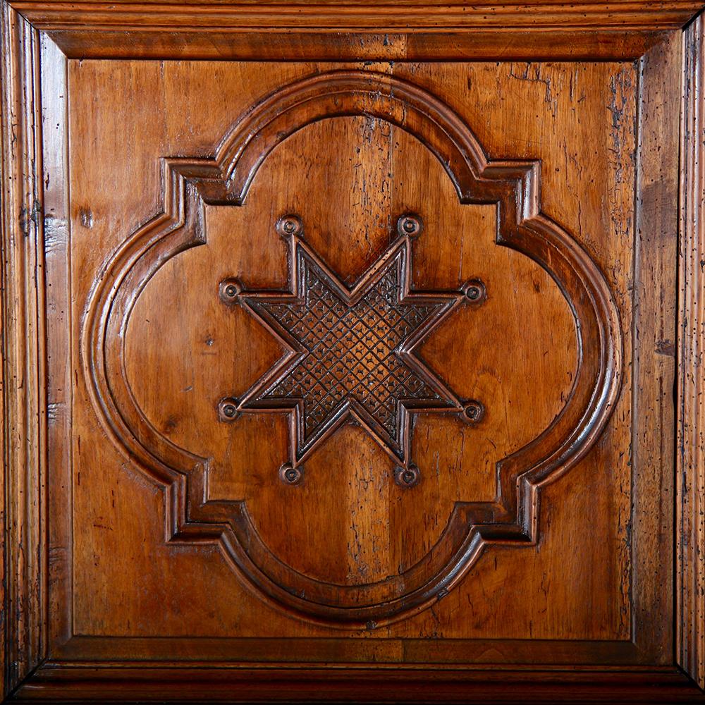 A late 18th-early-19th century French walnut two-door armoire with raised panelled sides and doors.
The arched-top doors feature three shaped panels with scrolled and curved molded borders, the middle panel on each door carved with an eight-pointed