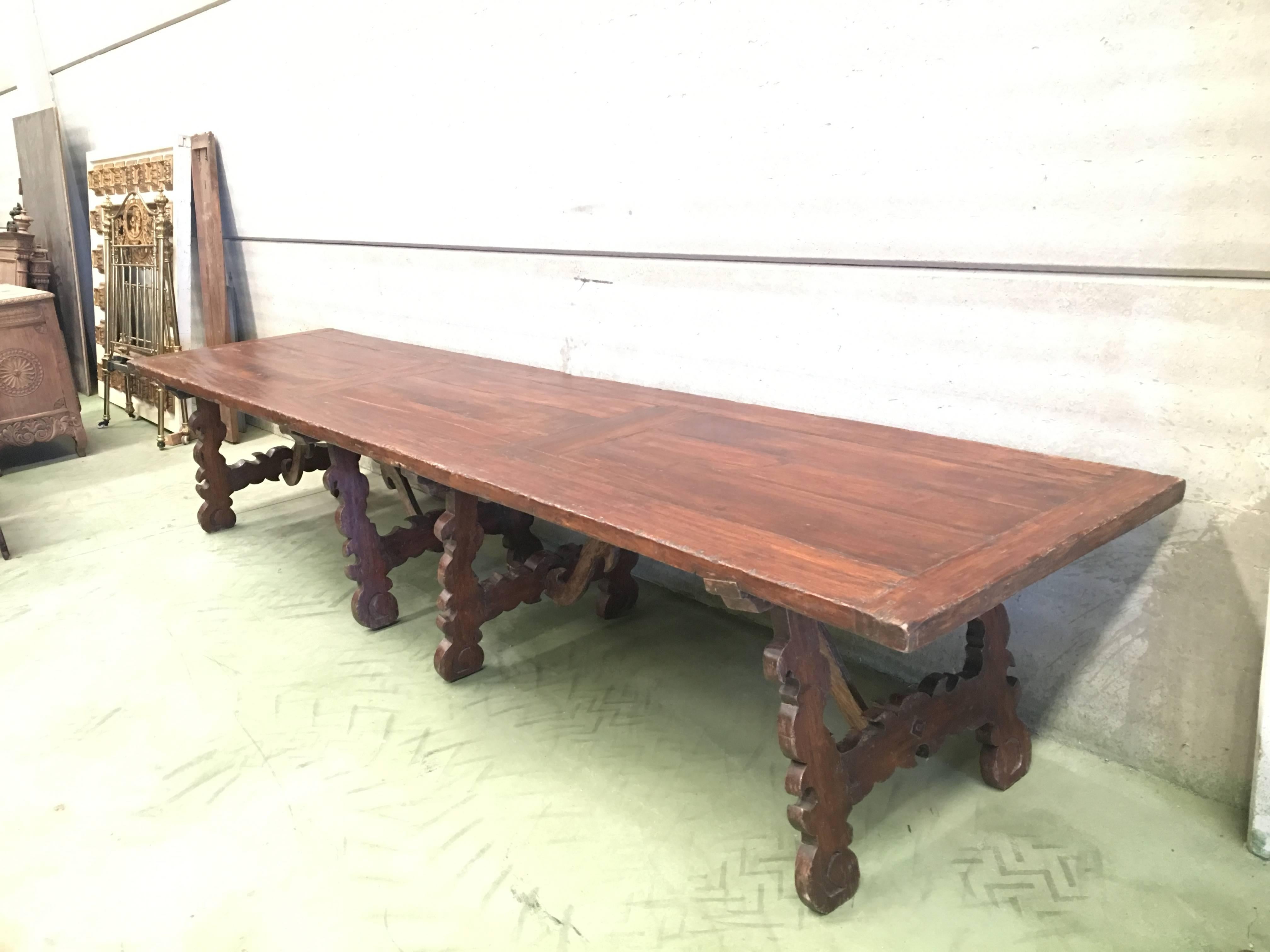 A monumental early 19th century Italian trestle table, having a rectangular framed solid walnut inset board top, resting on four hand-carved, classical lyre legs joined by four beautifully carved pair of wood S-scroll stretchers.

This table was