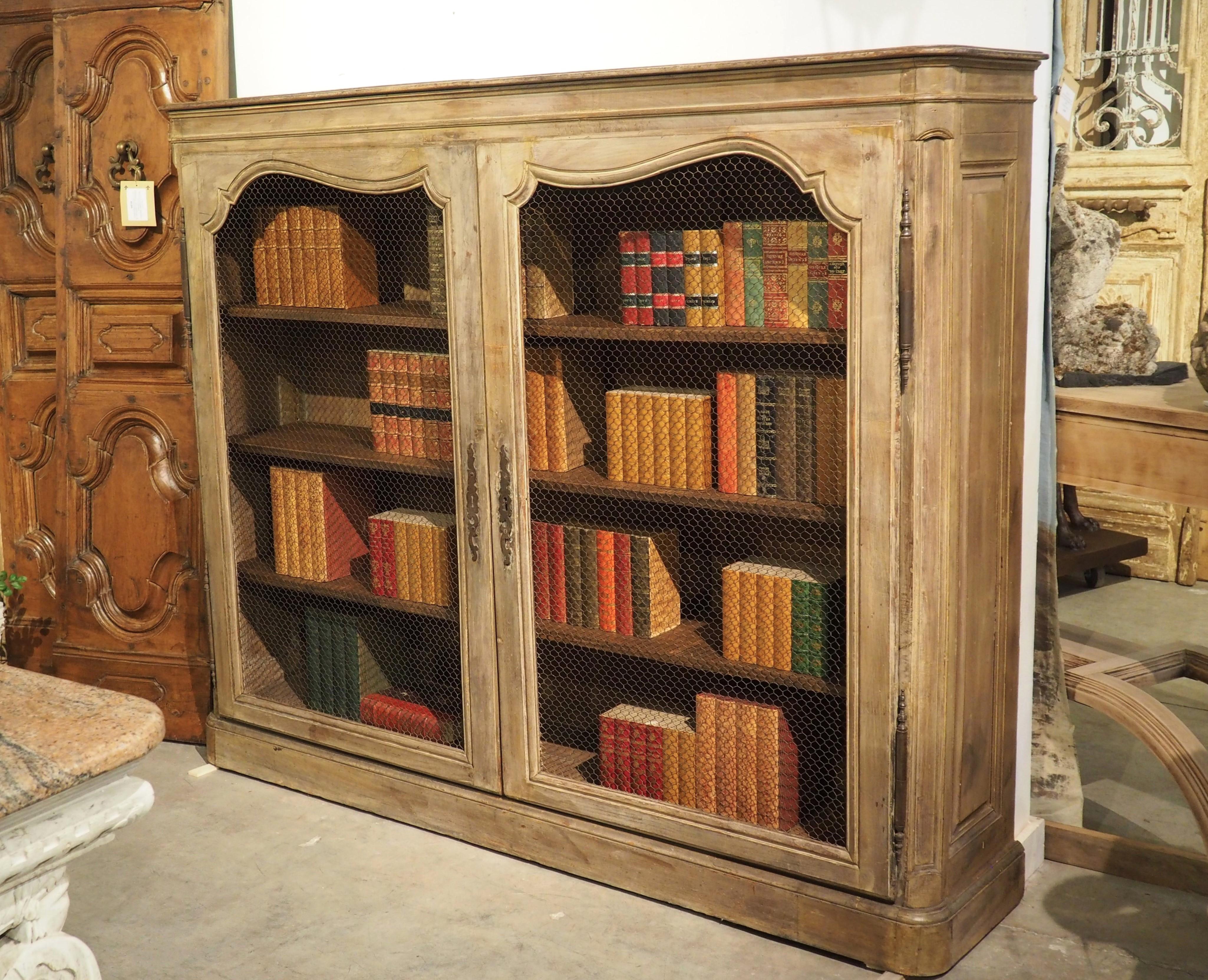 This handsome antique French bookcase or display cabinet features large doors with original chicken wire paneling, known as “grillage”, in French.  Most likely the upper section of a  large, 19th century French buffet a deux corps, this cabinet has
