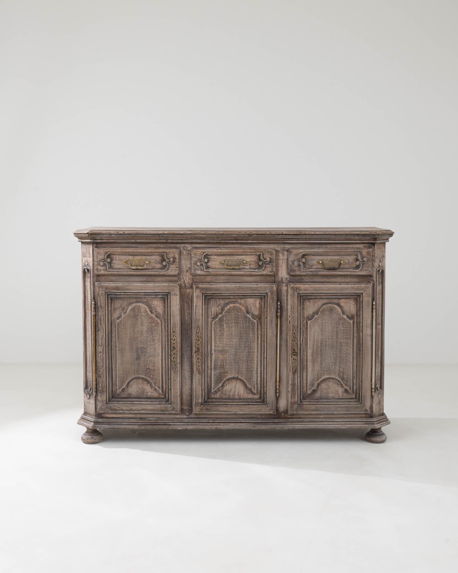 This early 19th Century French bleached oak buffet exudes a sense of rustic grandeur and timeless charm. The robust silhouette, defined by a sturdy plinth base and elegant molding, is softened by the gently weathered finish of the bleached oak,