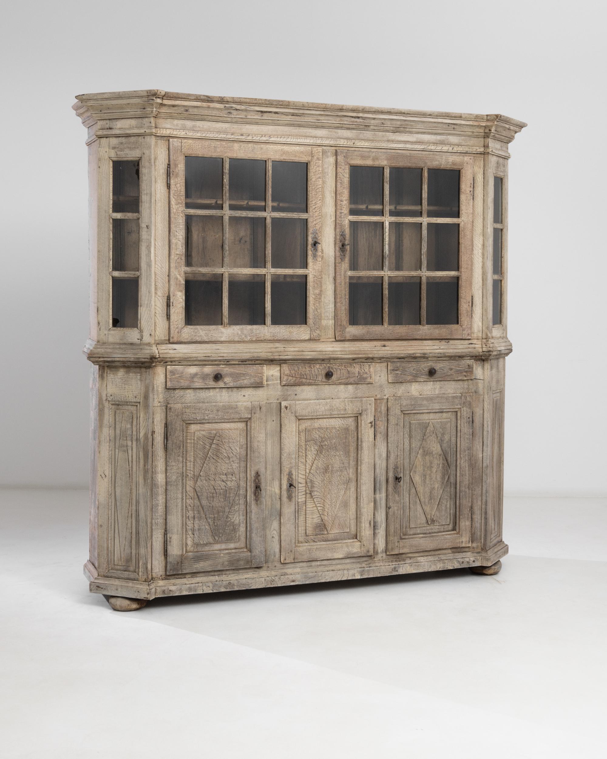 This spacious oak vitrine made in France circa 1800 has a remarkable faceted shape that provides extra storage space and gives the chest a peculiar silhouette punctuated by the geometric carvings on the panel doors and the molded cornice with