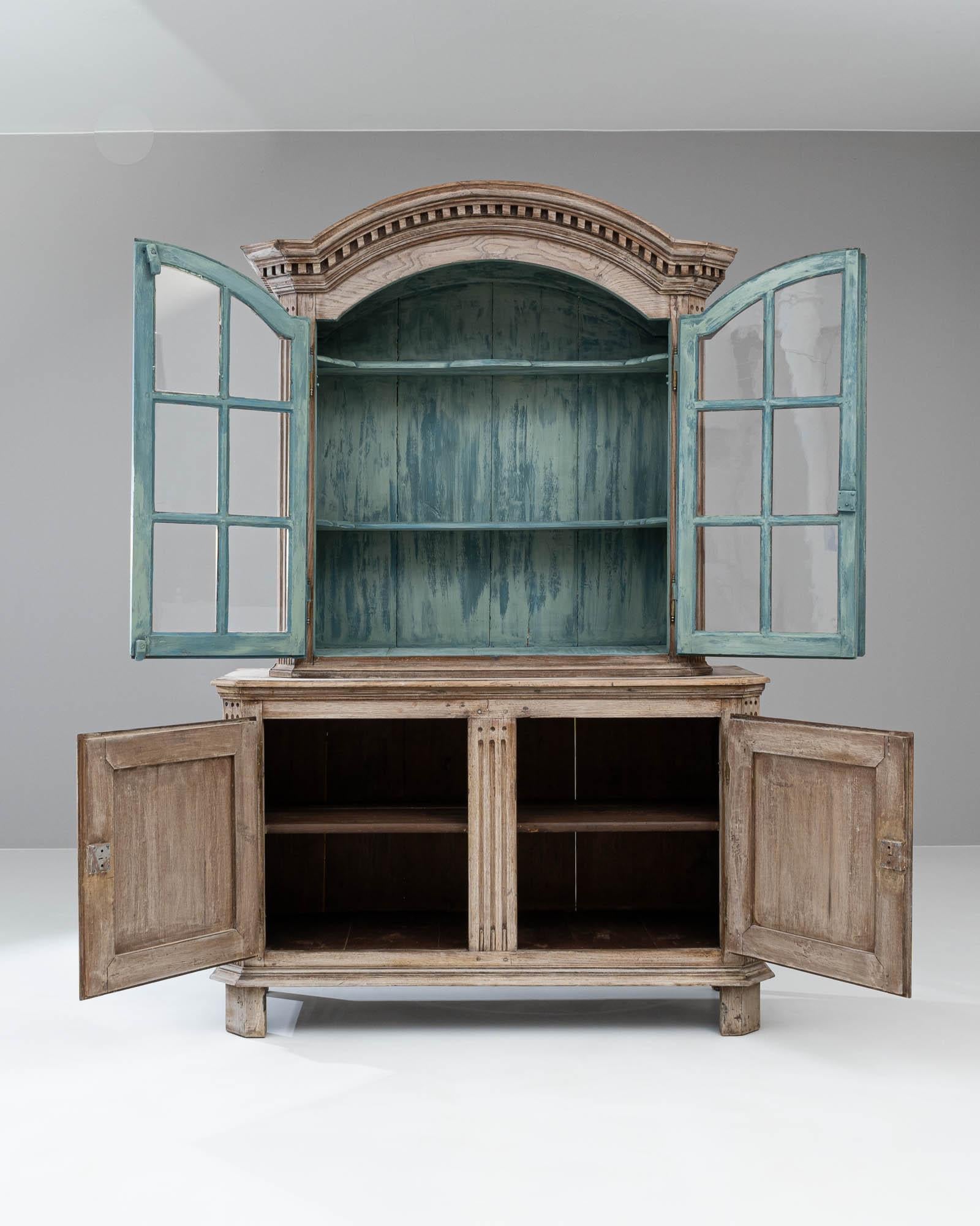 This grand 19th Century French Wooden Vitrine, with its stately presence and aged grace, stands as a testament to the timeless elegance of antique furniture. The cabinet's bleached wood façade is adorned with subtle carved details that reveal its