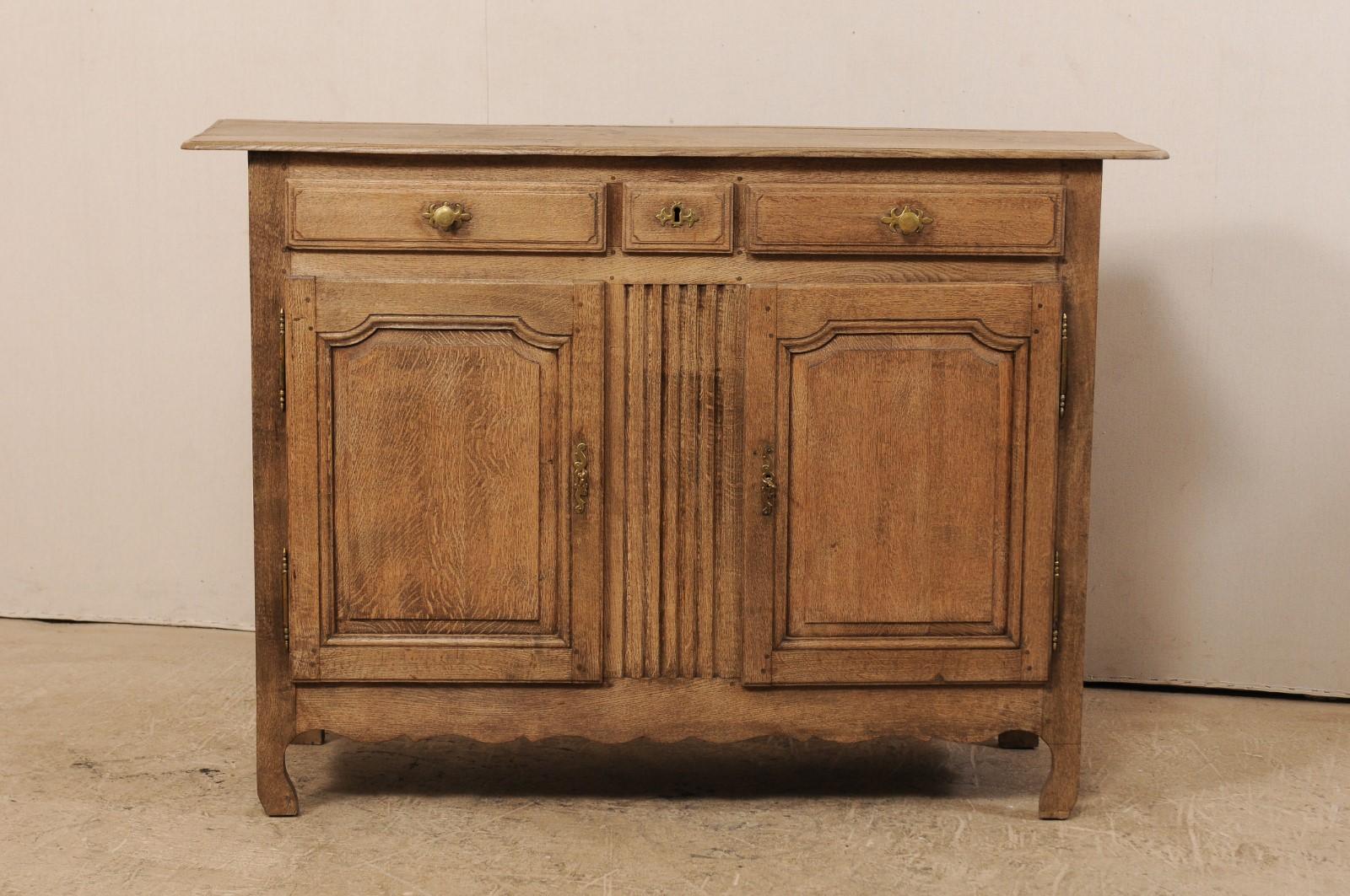 A French bleached oak buffet cabinet from the early 19th century. This antique cabinet from France features a rectangular-shaped top with rounded edges, above three panel-front drawers (a smaller center drawer flanked by a pair of longer drawers),