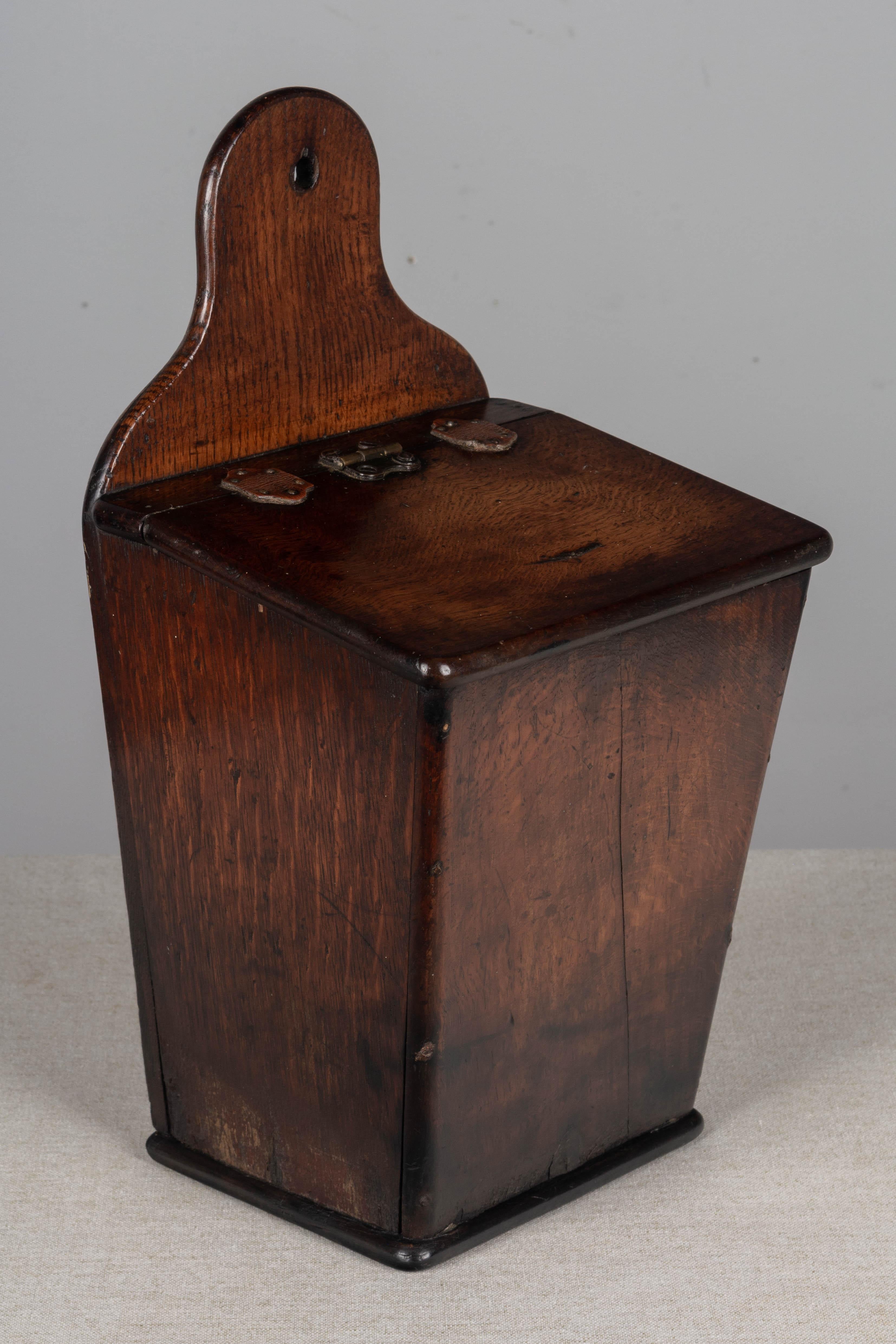 An early 19th century French boite à sel, or salt box, made of solid oak. Hinged lid with tacked leather tabs. A simple handcrafted box with nice proportions and beautiful patina. This box was used to store salt and would have been hung on the