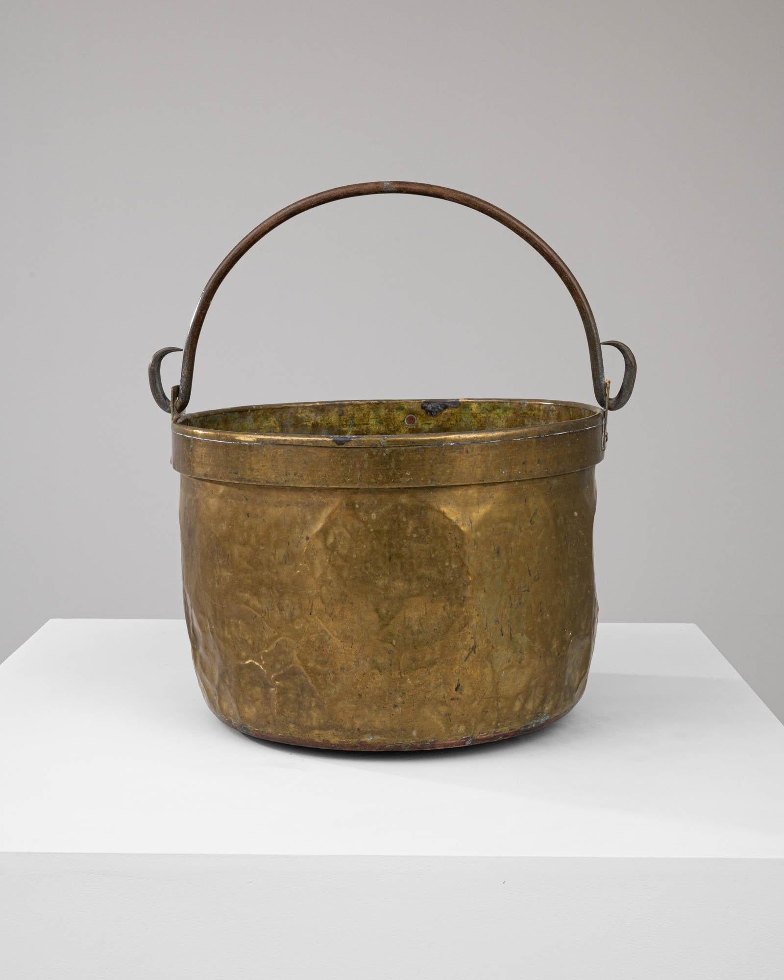 This Early 19th Century French Brass Bucket, with its full, rounded body and distinguished patina, is a striking example of traditional craftsmanship. The bucket, made from brass, has developed a rich, textured surface over time, evocative of its