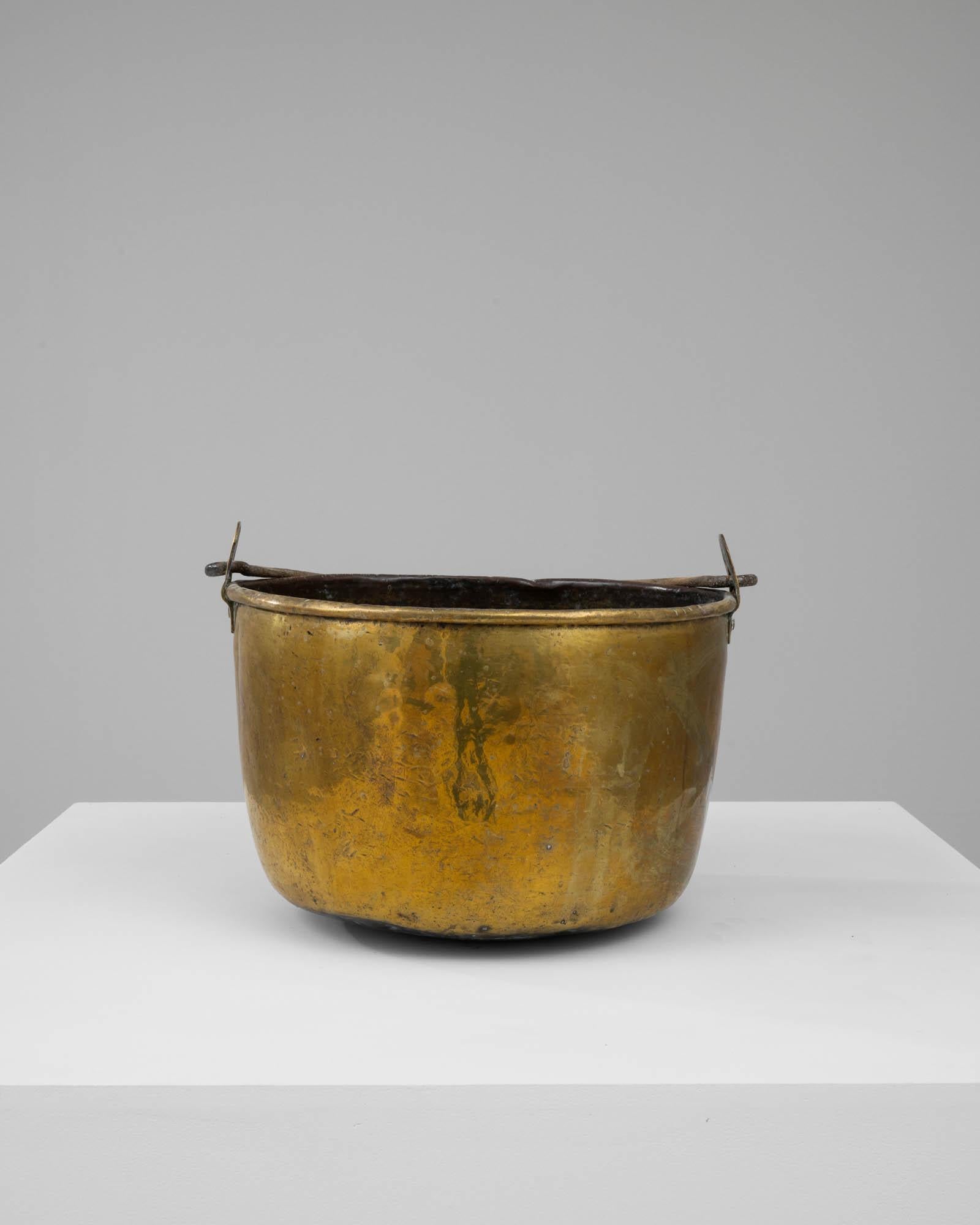 This Early 19th Century French Brass Bucket is an enchanting piece of functional history, evoking the everyday life and labors of the past. Constructed from brass, this bucket has acquired a warm golden patina over the years, bearing marks and