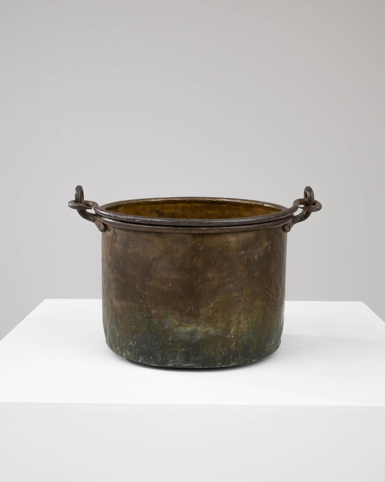 This French Brass Bucket from the early 19th century is steeped in historical value, having served countless purposes over many decades. The iron handle, exhibiting an elegantly simple twist at its apex, is a functional design element that adds a
