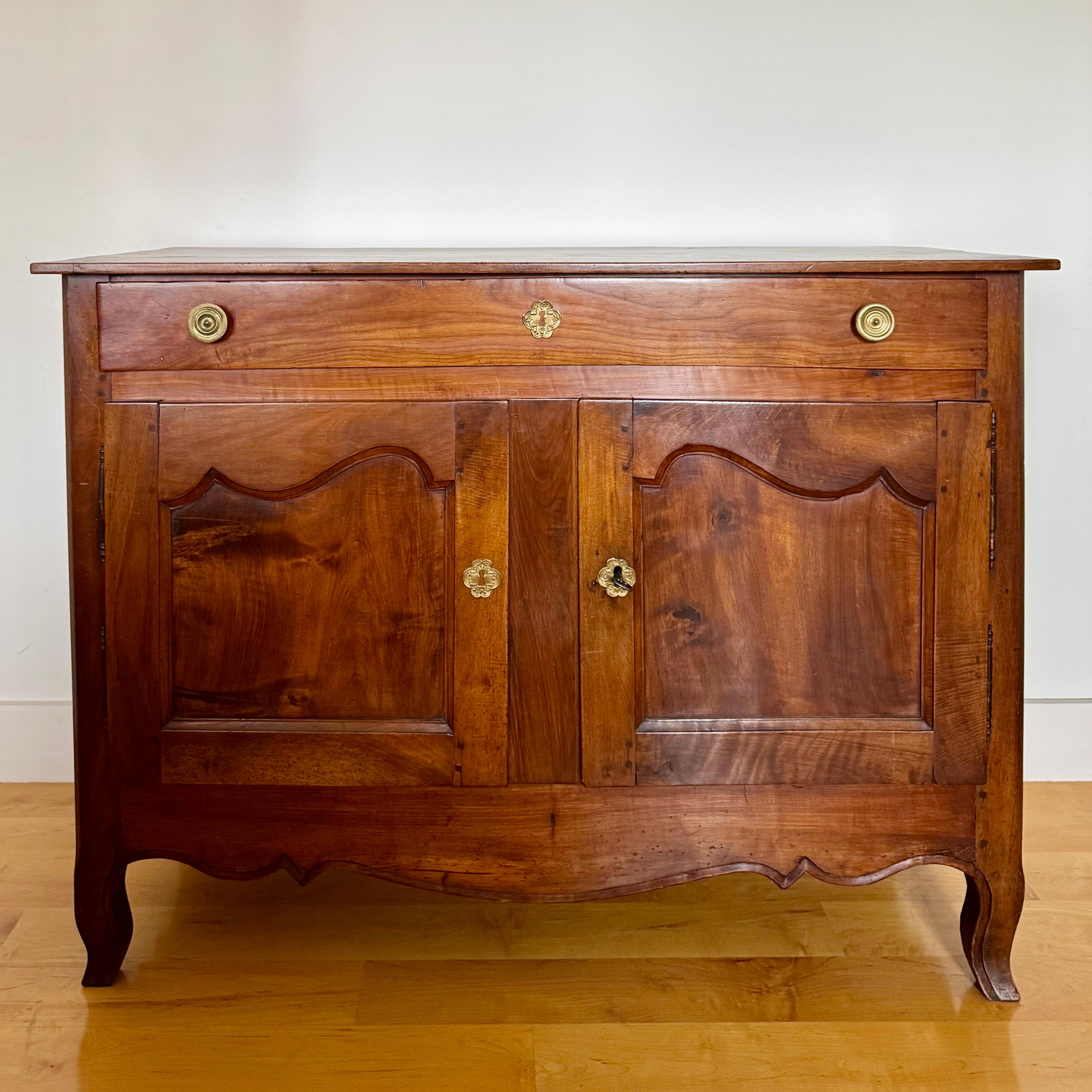 Magnificent French early 19th century carved walnut Provençal buffet with one long drawer and two cabinet doors with a chapeau de gendarme form, carved  apron, bronze escutcheons, hinges and original lock resting on beautiful scroll feet.
