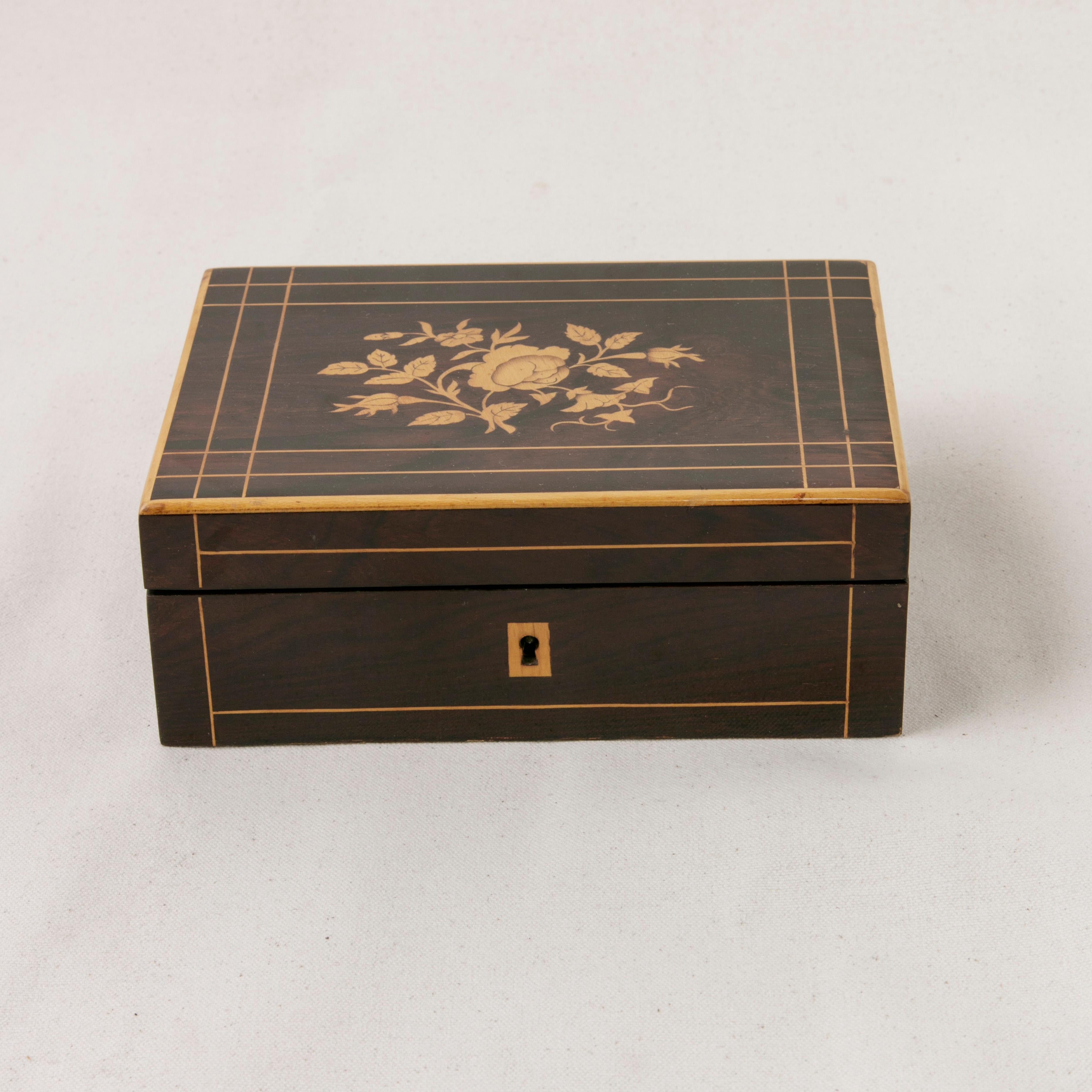 This early 19th century French Charles X period palisander box features a finely inlaid lemon wood border on its top and front. An inlaid central floral and leaf motif decorates the top. Used as a traveling sewing kit, this box includes all of its