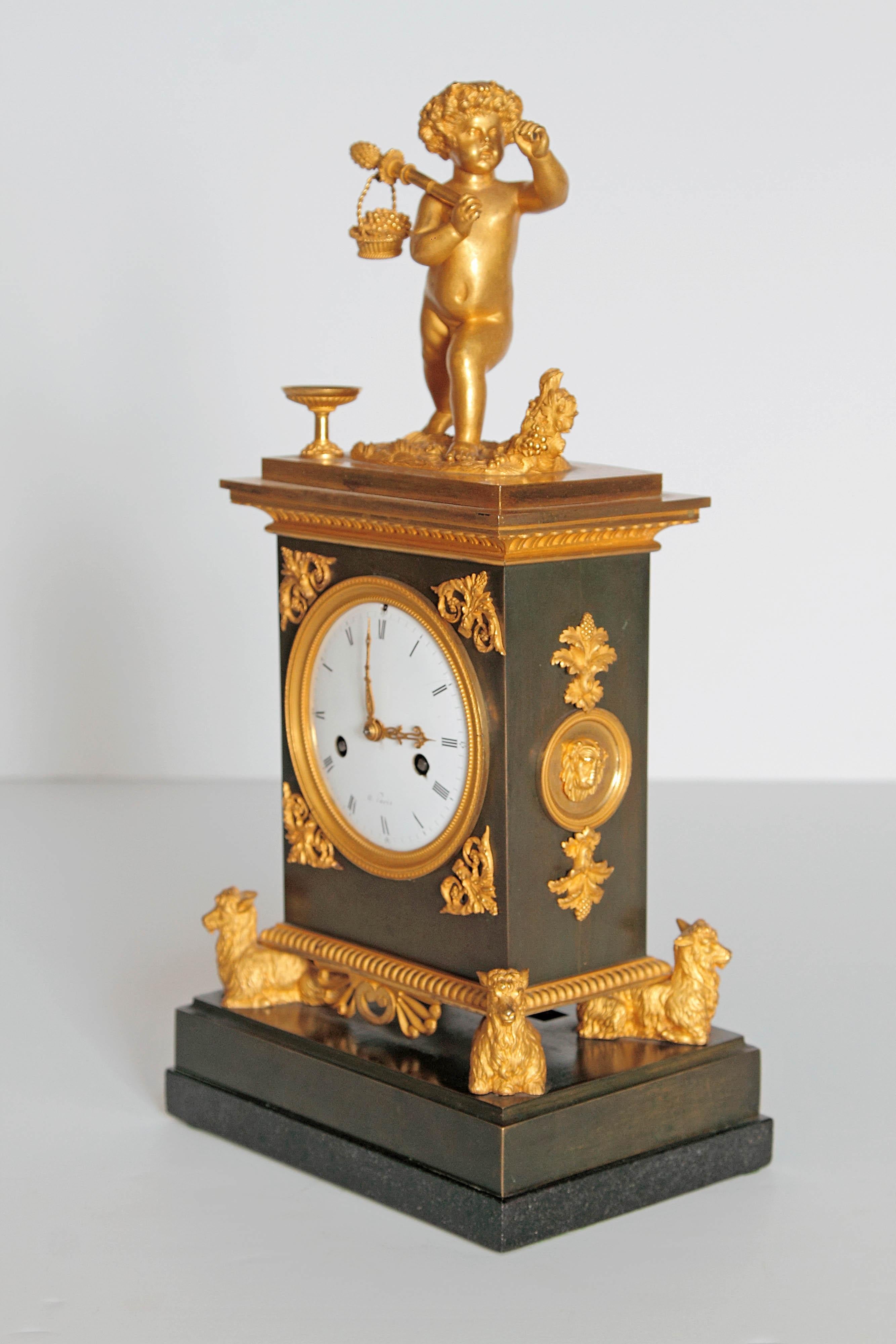 An elegant French black marble clock with gilt bronze embellishments. Four gilt goats on base support the clock. Gilt mounts on sides have lions heads. A large putto with basket of fruit is on the top, enameled round white face. Early 19th century,