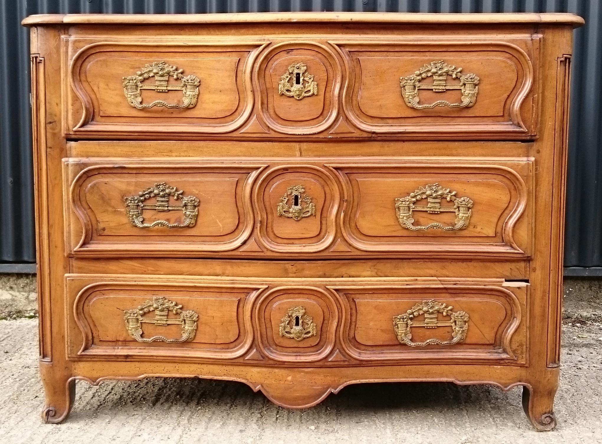 Early 19th century French antique commode chest with three drawers. This is a very decorative chest of drawers typical of the period, with carved serpentine front, lovely big brasswork handles and escutcheons and shapely outsplayed feet.
The timber