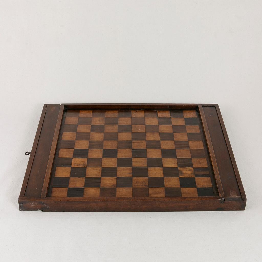 This early 19th century walnut and ebonized pear wood marquetry game board is double sided and features a chess and checker board playing surface on one side and a more traditional 10 x 10 draughts board on the other side. Two sliding compartments