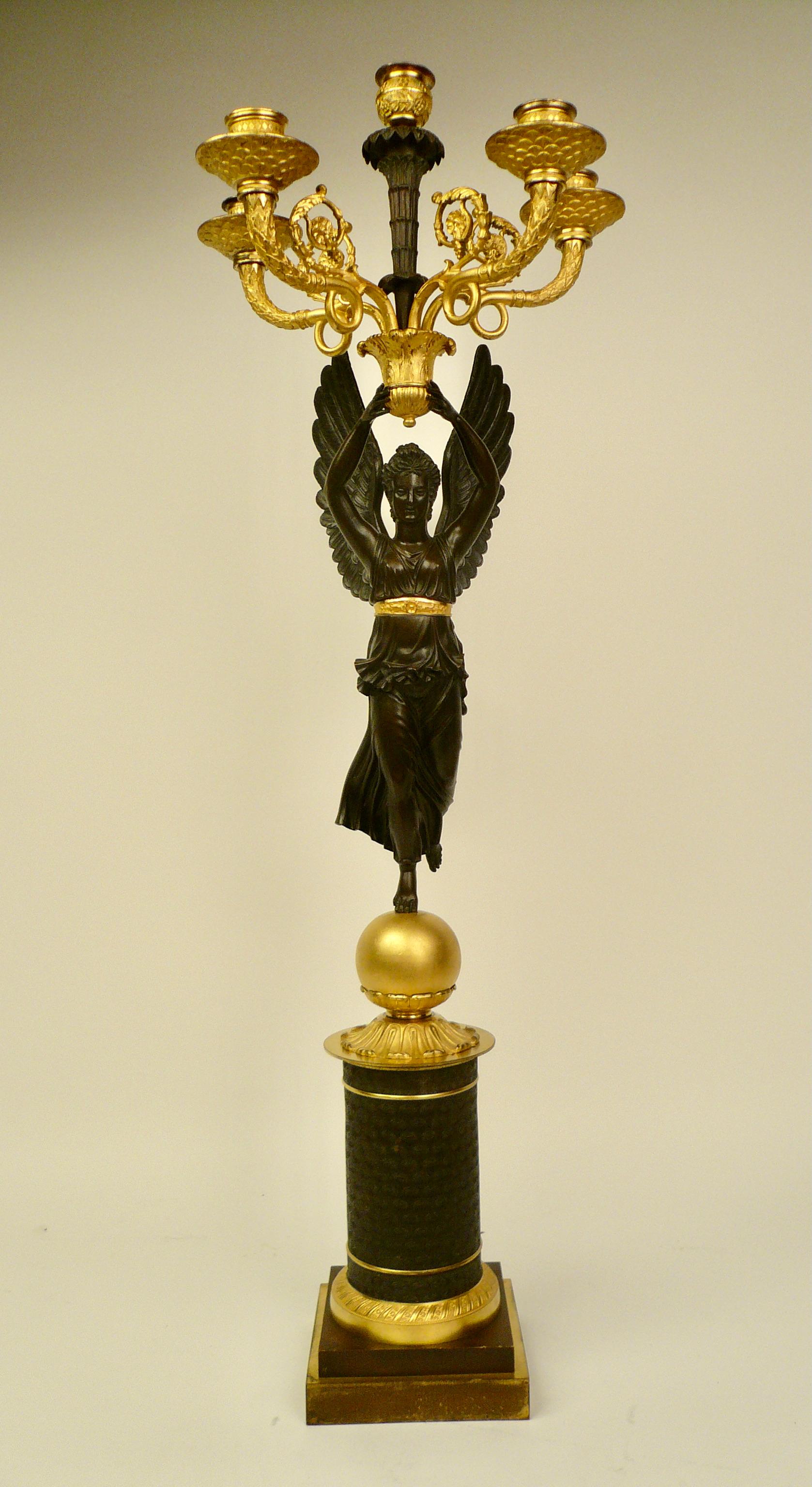This stately patinated and fire gilt bronze candelabrum is of the finest quality, and retains its original finish.
The figure of Nike (Winged Victory) standing on a gilt globe holds aloft a five light candelabrum.
       