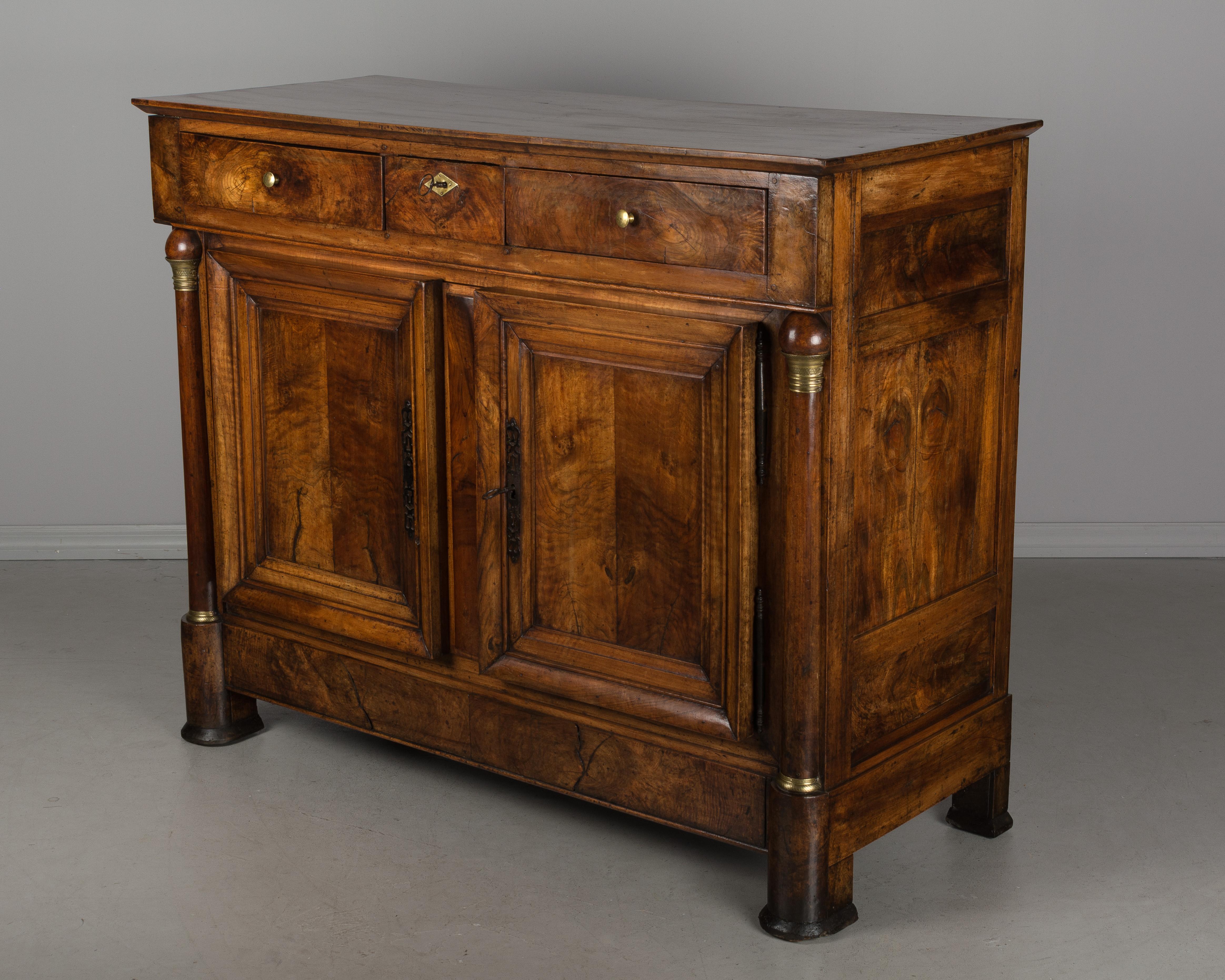 A large early 19th century French Empire Period buffet made of solid walnut from the Burgundy Province. Bronze mounted columns flank thick book-matched panel doors. Three dovetailed drawers. Working locks and two keys. The sides each have three