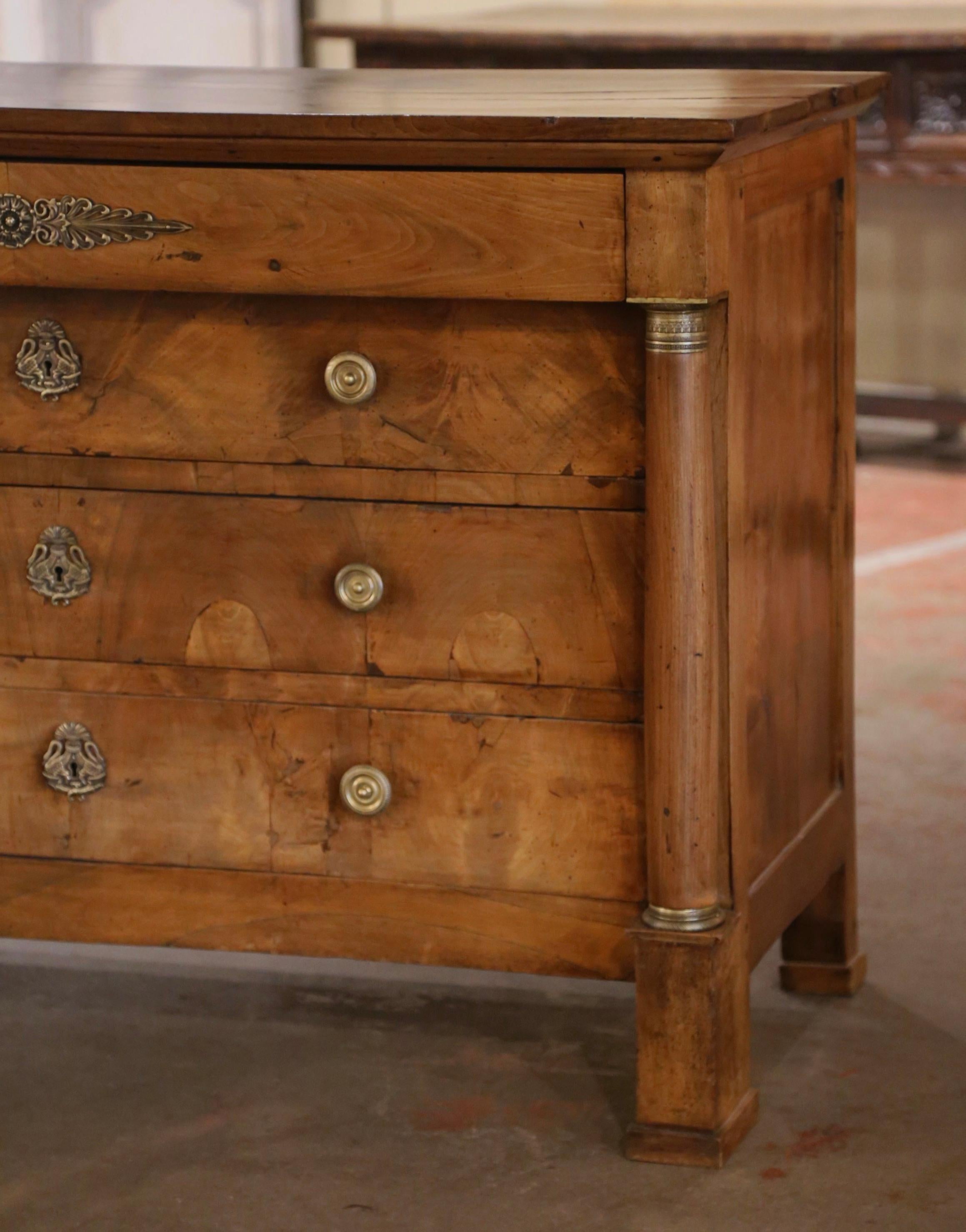 Questa elegante cassettiera in legno di frutta è stata realizzata in Francia, intorno al 1830. La tradizionale commode antica poggia su spessi piedi quadrati su colonne arrotondate decorate con anelli di bronzo in alto e alla base. Il mobile è