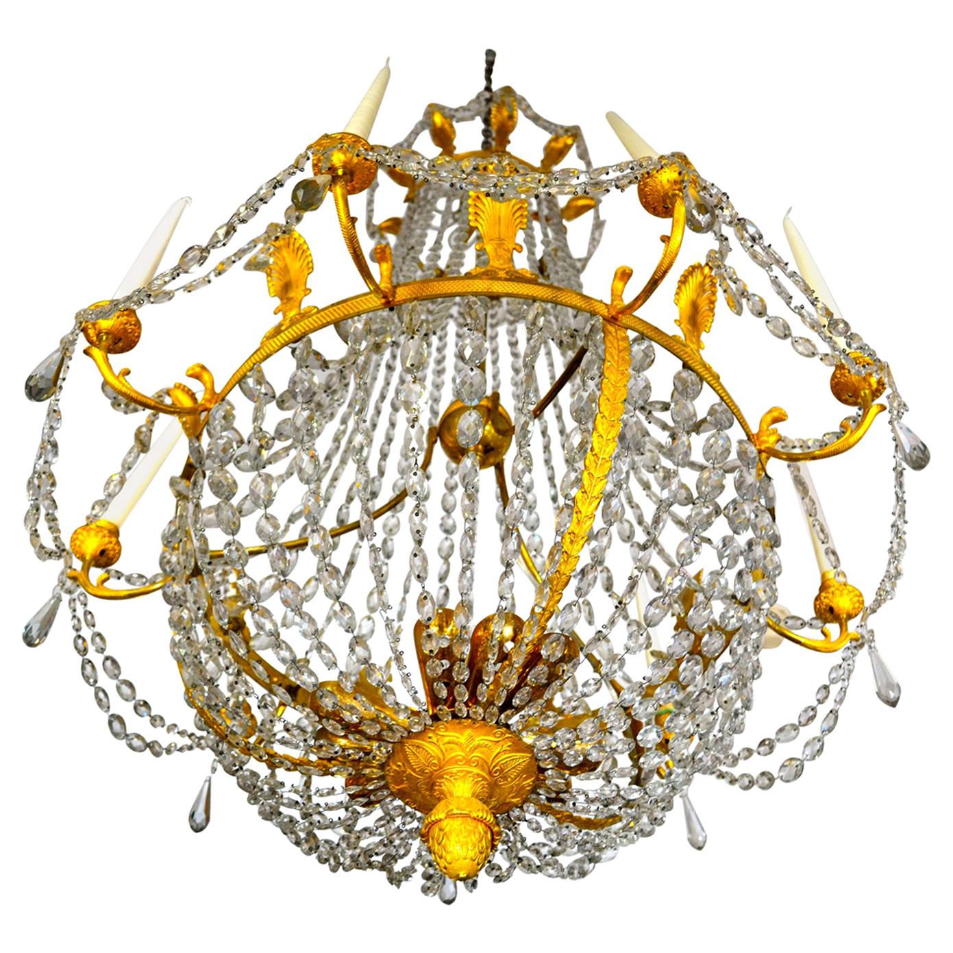 A period French Empire crystal and gilt bronze nine candle bell shaped chandelier of the highest quality; the circular corona surmounted by palm shaped finials suspending swagged crystal chains supporting a cascade of crystal drops to a main finely