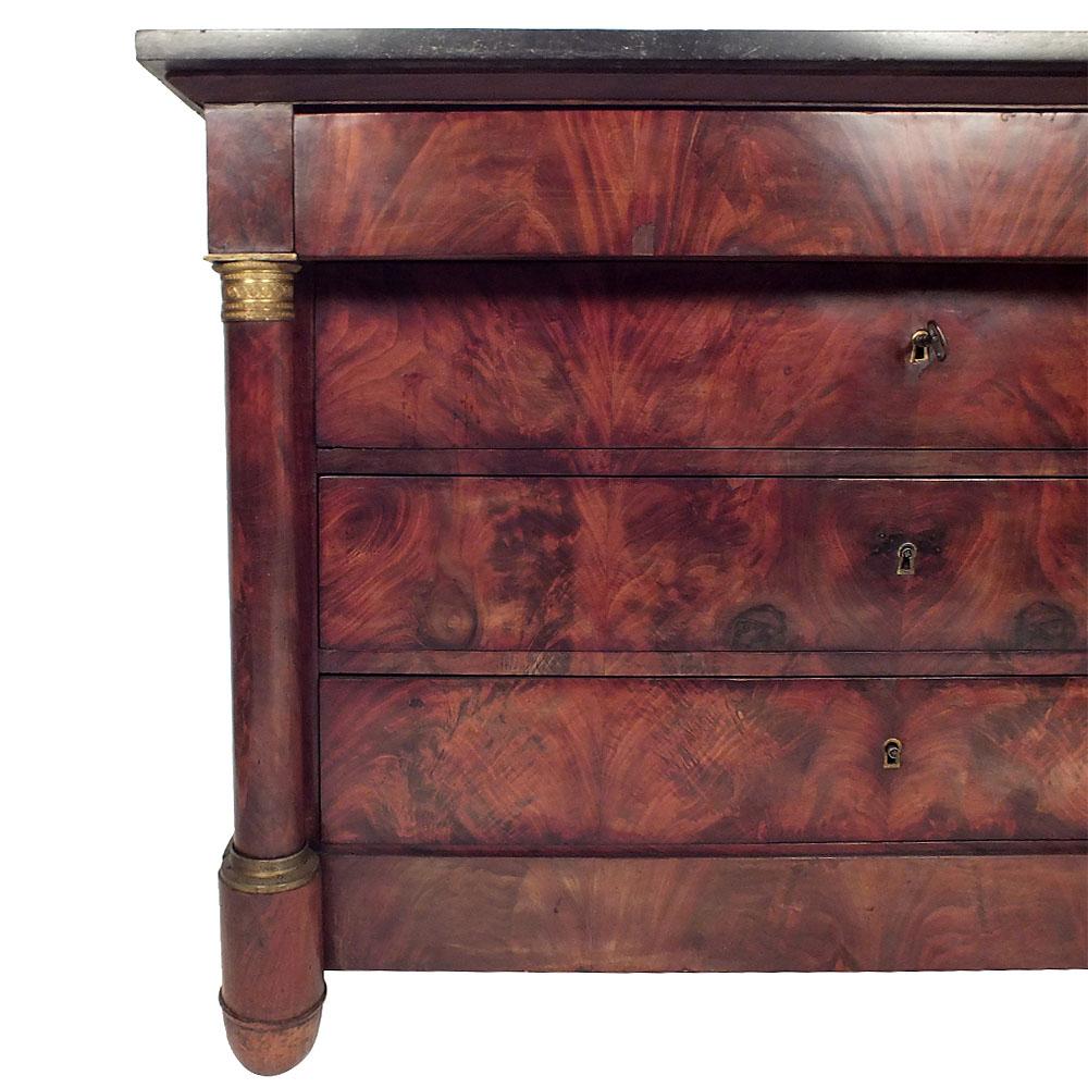 This is a beautiful 1840's French commode with a black marble top is made of solid wood covered in Flemish mahogany veneers. It has turned columns with bronze capitals and base rings on the sides, four drawers with keyholes., and lock and key in