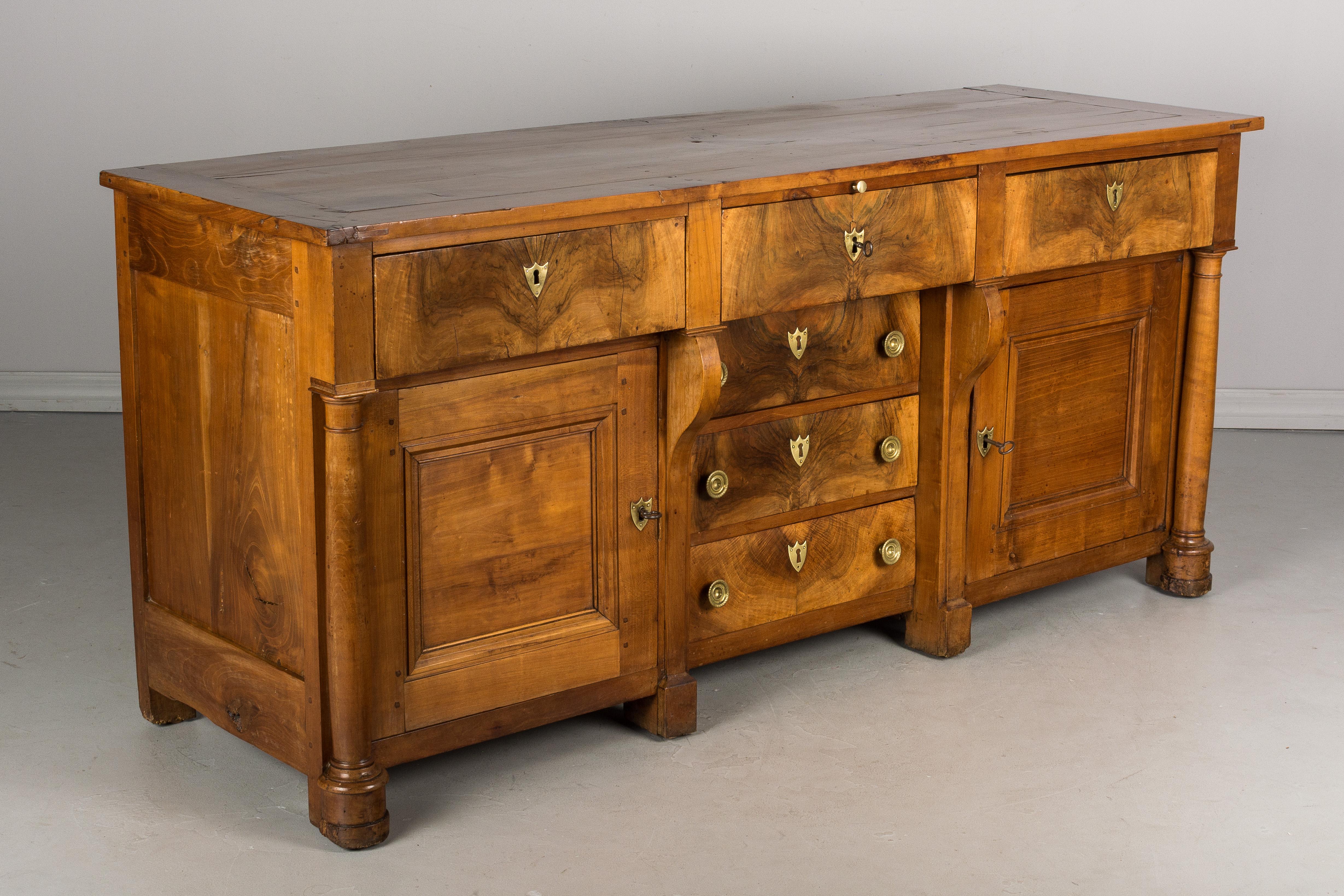 An early 19th century French Empire Period enfilade, or sideboard, made of solid cherry. Six deep dovetailed drawers faced with 1/4 inch thick book-matched walnut veneer. Solid cherry panel doors on either side flanked by turned columns. Pull-out