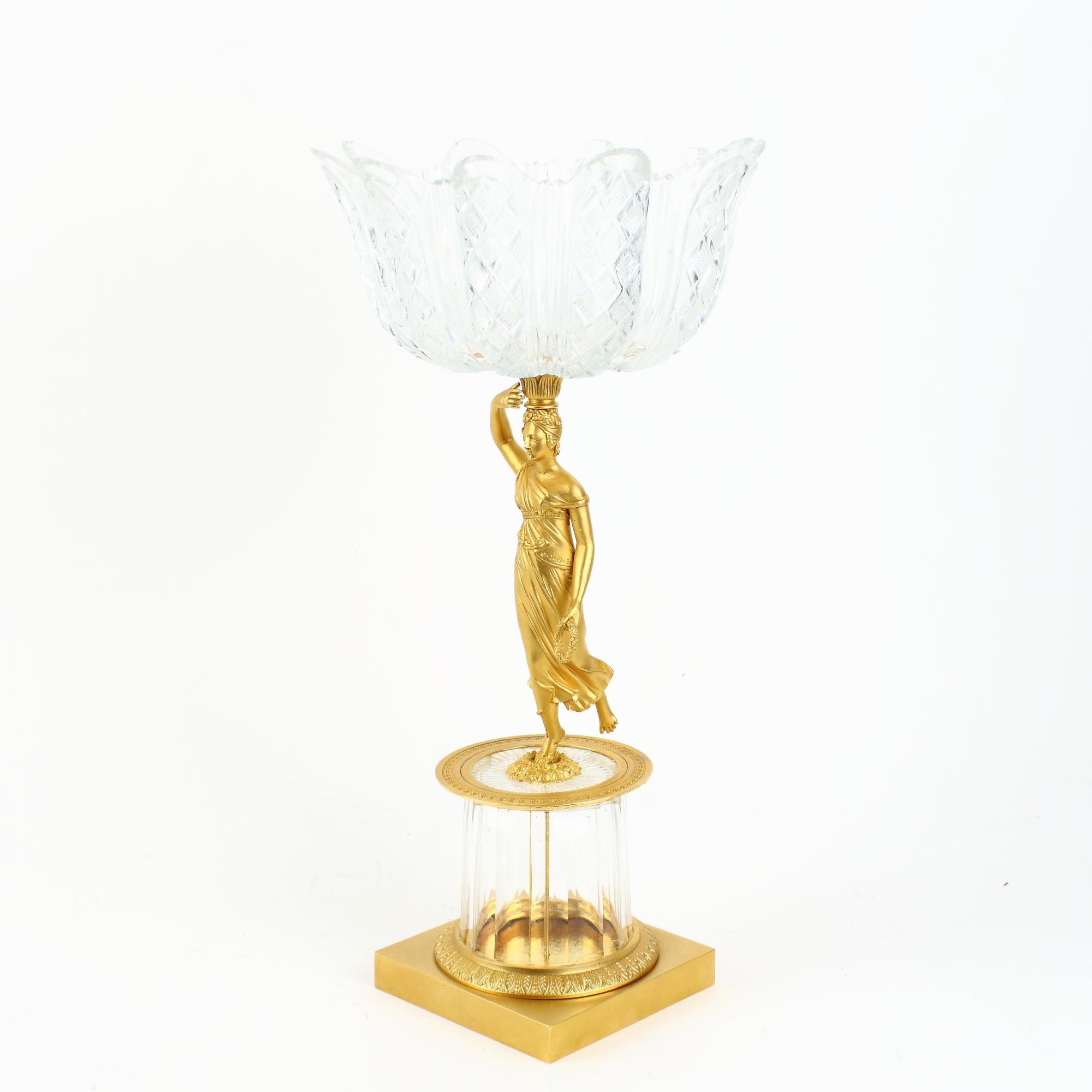 Early 19th century French empire gilt bronze and glass figural tazza or bowl.

A gilt bronze figure of a young female wearing an ancient Greek style peplum standing on a round faceted crystal glass base with a gilt bronze plinth. The figure is